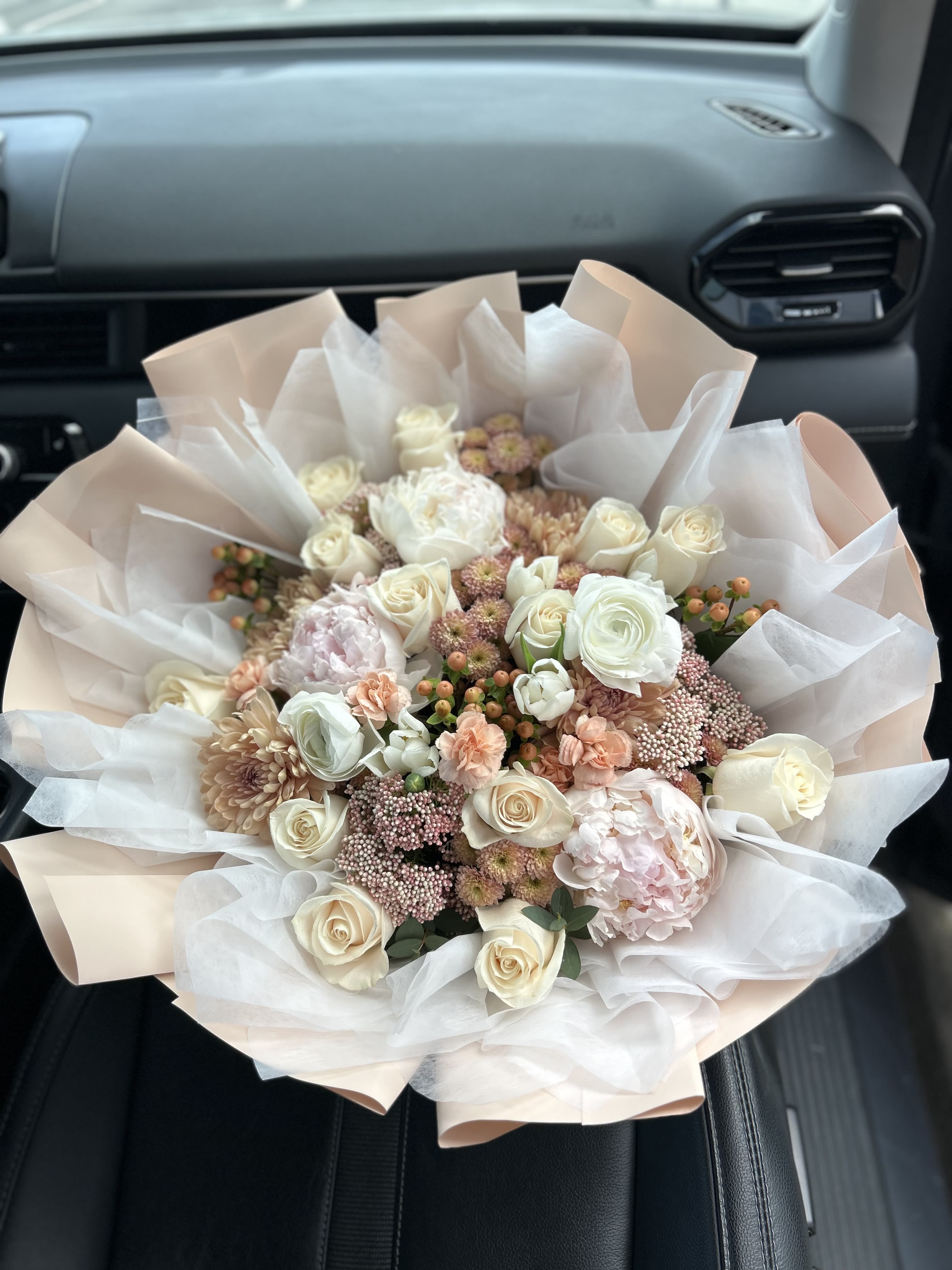 Bouquet of cream and blush roses with pale pink flowers wrapped in white paper