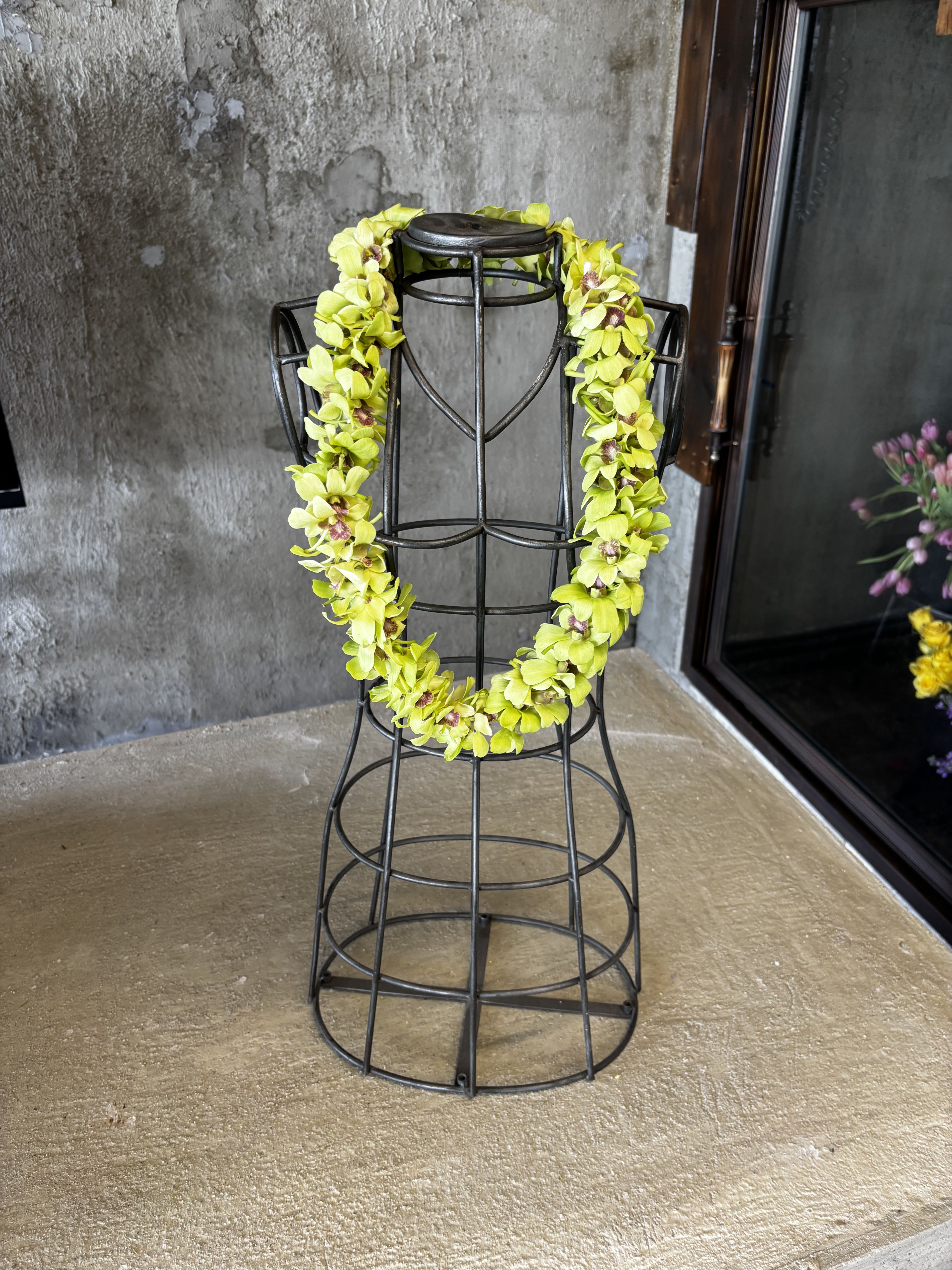 Yellow orchid lei draped over a black metal dress form
