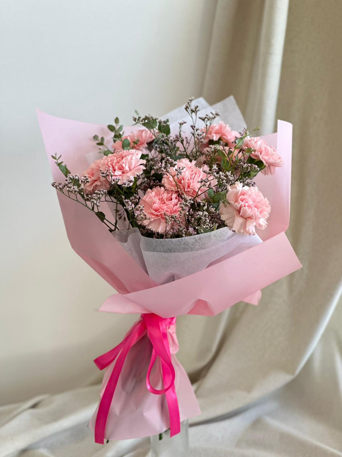 Pink carnation bouquet wrapped in pastel paper with a ribbon