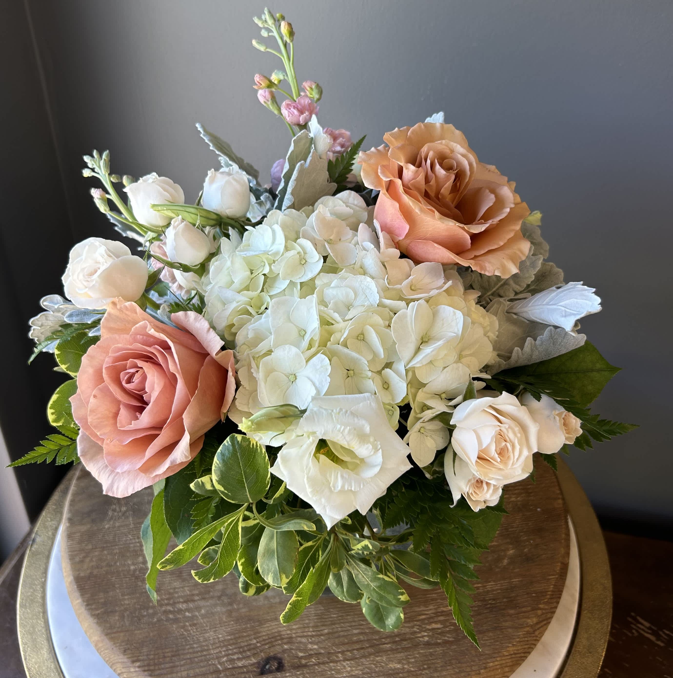 Low arrangement of white hydrangeas with peach roses and white accent blooms in a rounded design