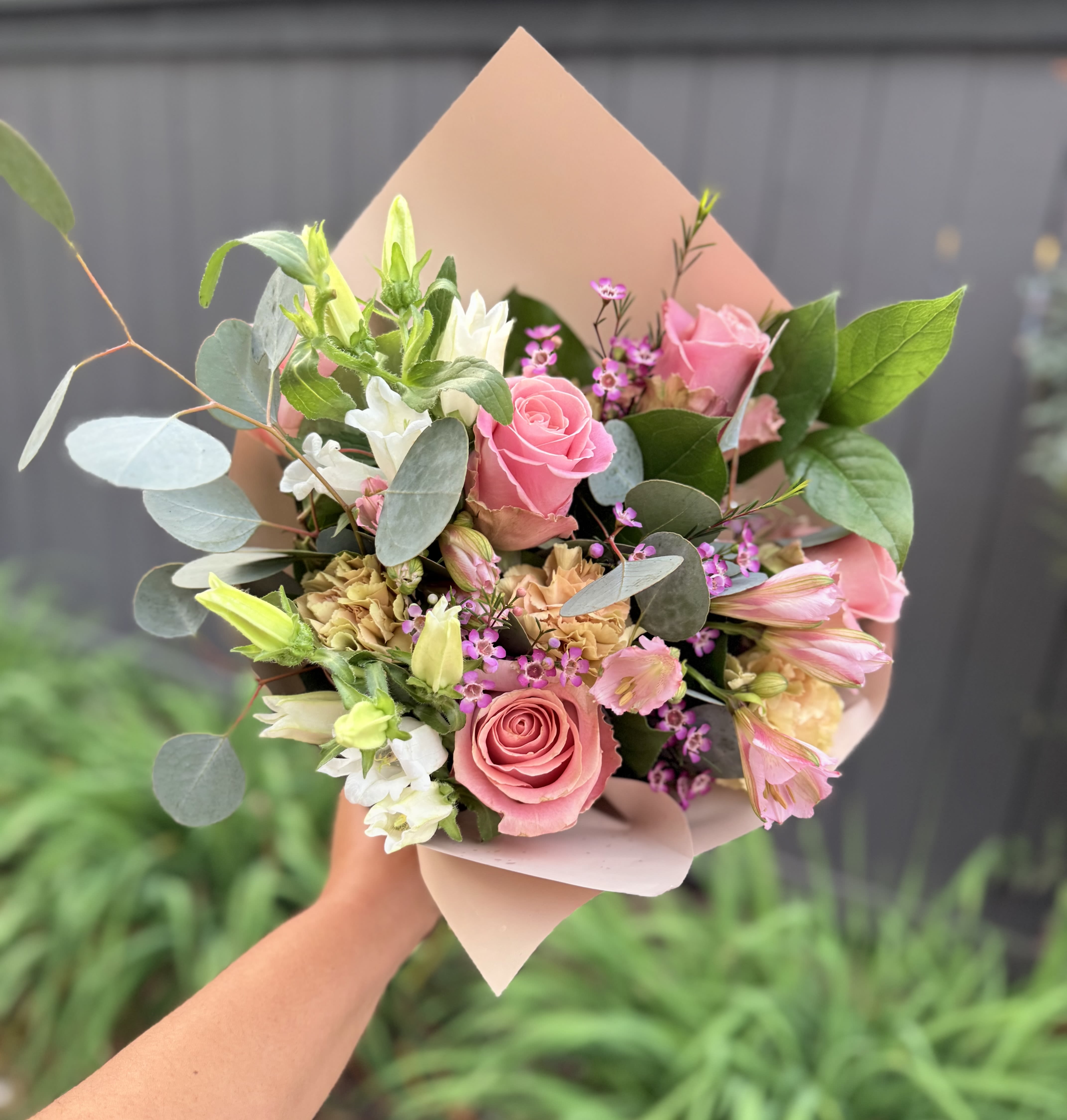 Handheld bouquet of pink roses, white blooms, and eucalyptus in blush wrap