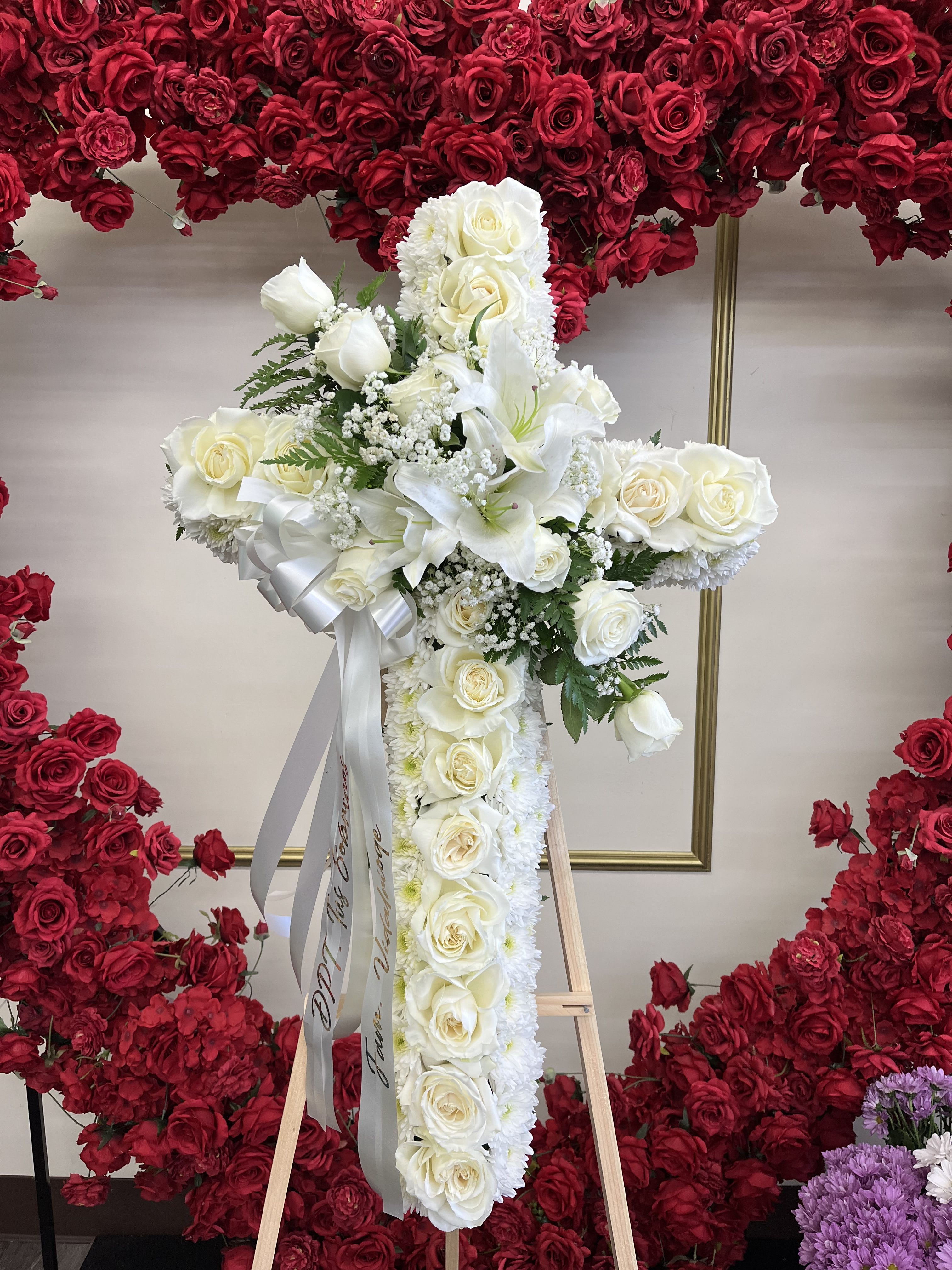 White floral cross arrangement on an easel with red rose backdrop