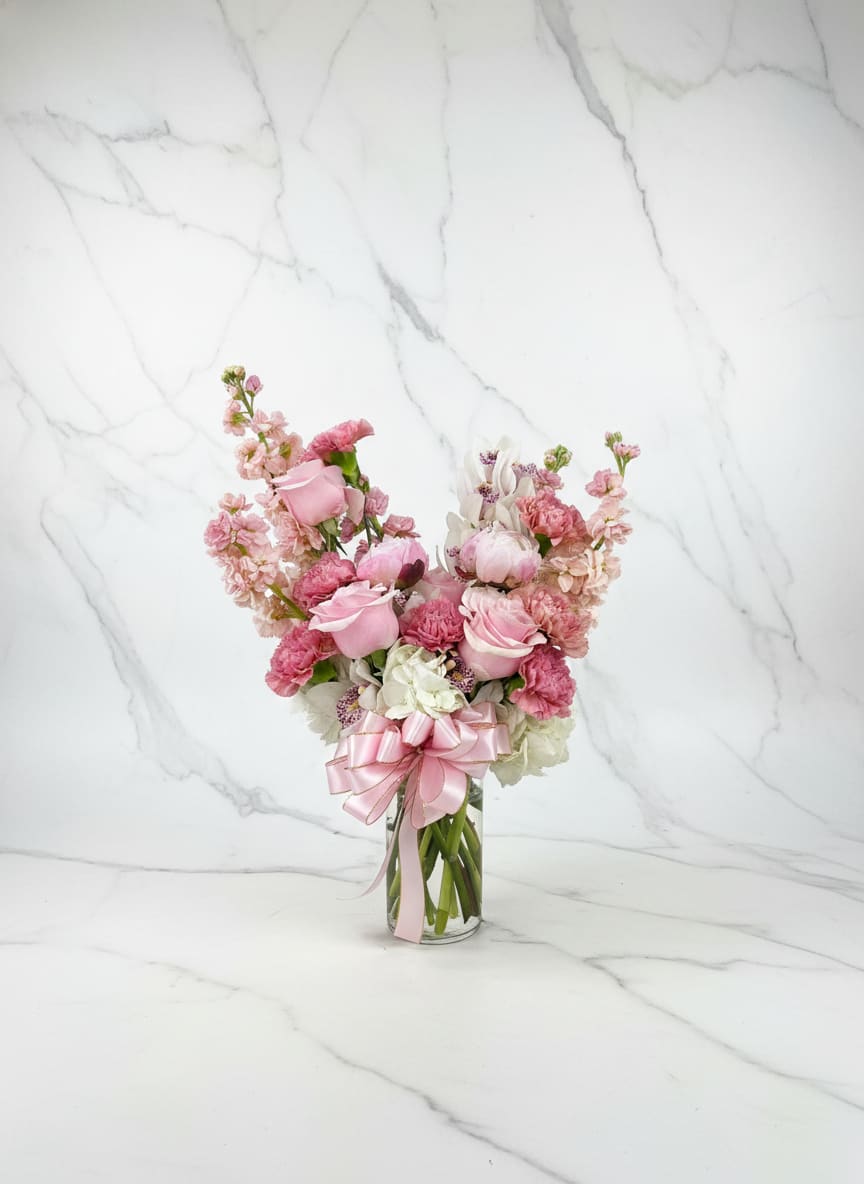 Lege Cymbidium Vase - A soft and elegant vase arrangement featuring white hydrangea, peach stock, lege pink carnations, peonies and pink roses. At the center, a striking cymbidium orchid serves as the focal bloom, adding a refined and modern touch. This design blends delicate textures and warm tones, making it perfect for any special occasion or as a statement piece.
