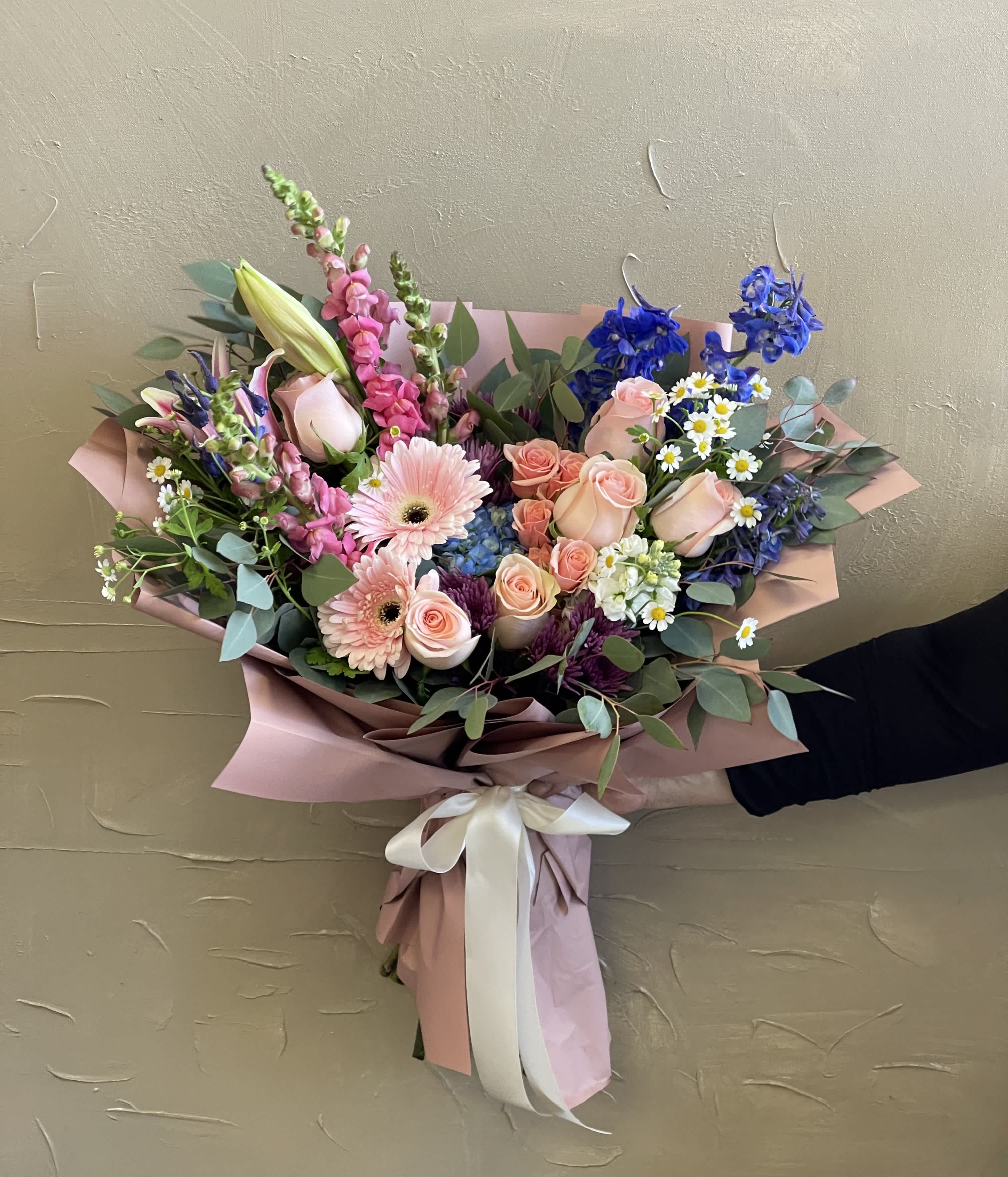 Hand-tied bouquet of pink roses, gerbera daisies, and blue flowers in pink wrap