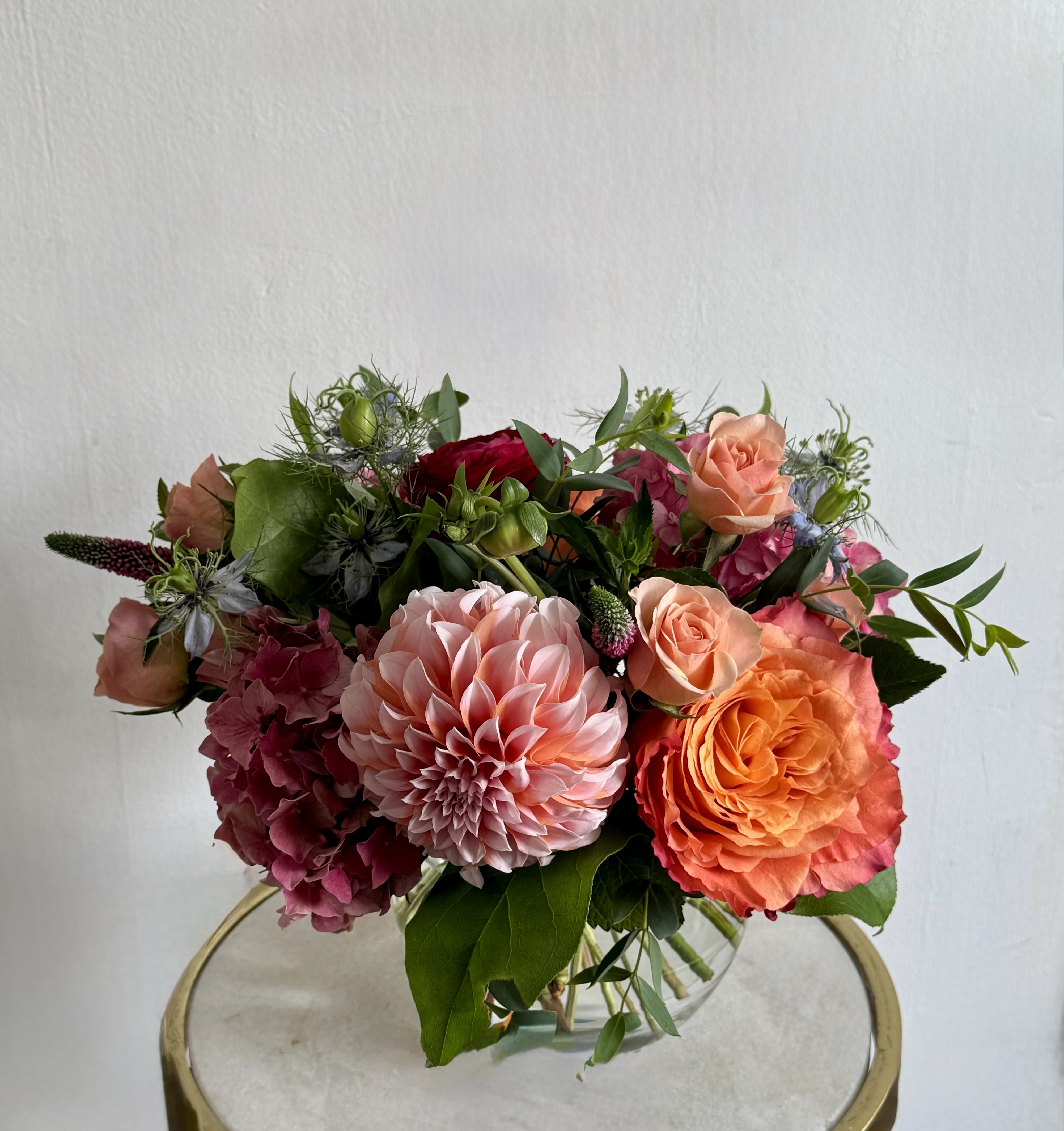 Mixed bouquet with pink dahlias, orange roses, and magenta hydrangeas in a glass vase