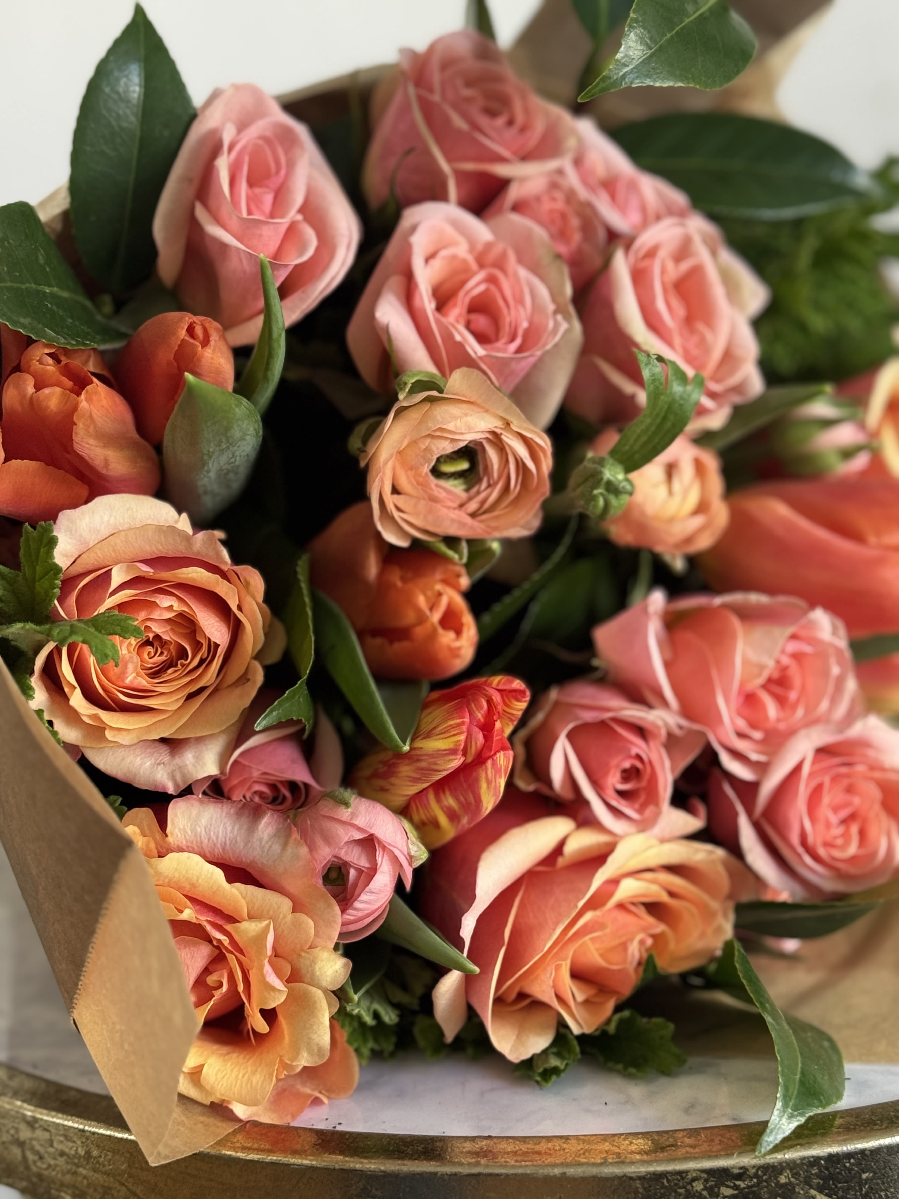 Pinky Orange DESIGNERS CHOICE  - A lush, hand-tied bouquet of pink, peach, bright orange-coral  that reads like a warm, joyful embrace-perfect as a birthday bouquet, anniversary flowers, or a general celebratory gift for the person you're thinking of. The mix of these colors creates an energetic mood that says "I'm celebrating you" without being over the top.  Tightly clustered blooms are arranged in a market-style wrap of natural brown paper for a casual, artisanal finish that feels personal and modern. Hand-delivered in its brown paper wrap, this bouquet is ready to brighten a table or bedside; to keep blooms fresh, trim stems and place in clean water upon arrival.