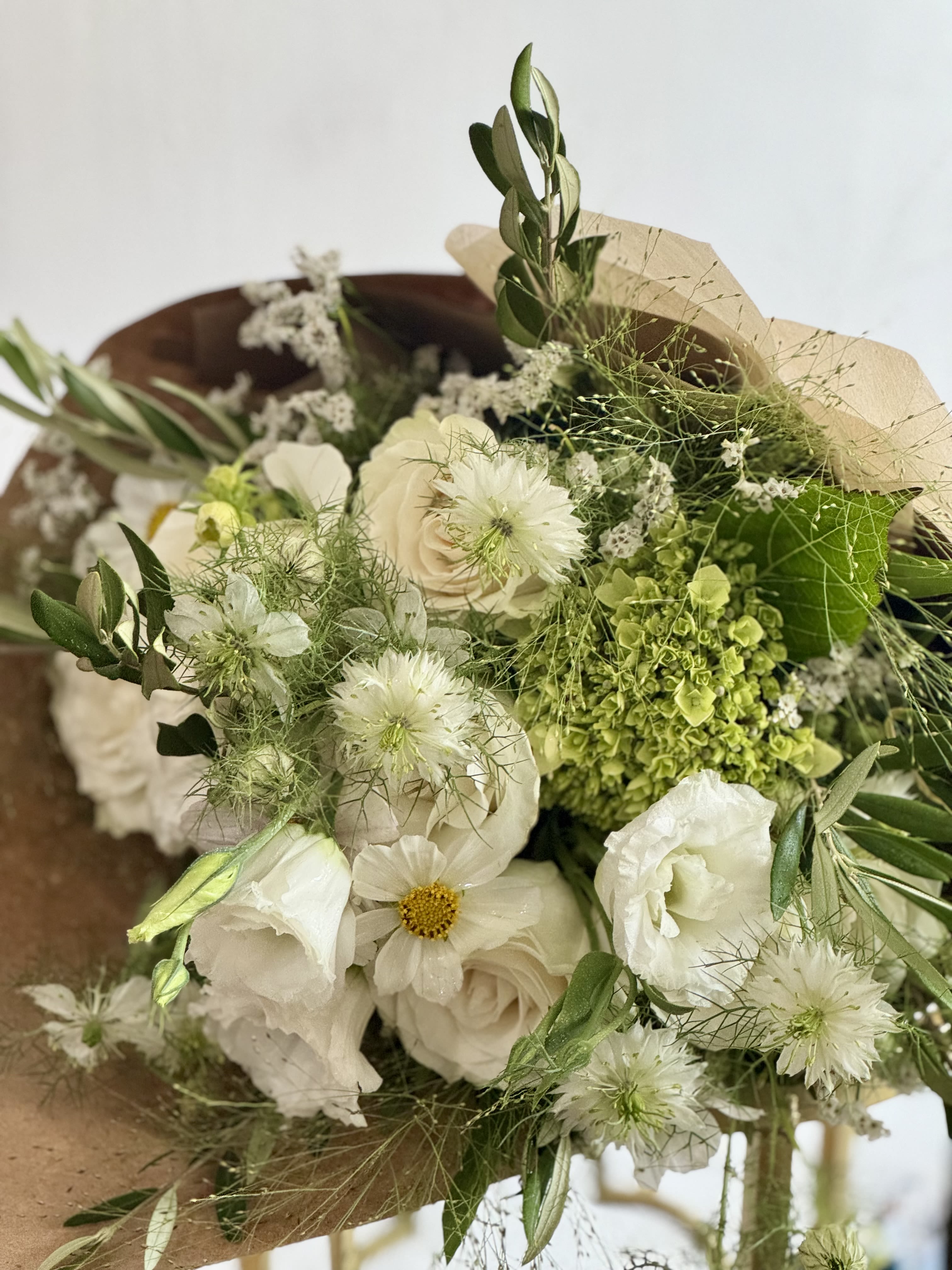 Green + White DESIGNERS CHOICE - The gentle mix of white  and fresh green foliage gives the arrangement an airy feel that will make the person you're thinking of feel truly seen and cherished. Hand-tied bouquet. Paper wrapped. Designers Choice   This generous arrangement layers pink, white and green. Sized to read abundant and garden-fresh, it arrives loose and tactile - simple care (fresh water and occasional stem trims) keeps the blooms looking their best. Orders are designer's choice to guarantee the freshest premium flowers for Mother's Day, funerals, thank-you gestures, or everyday celebrations. 