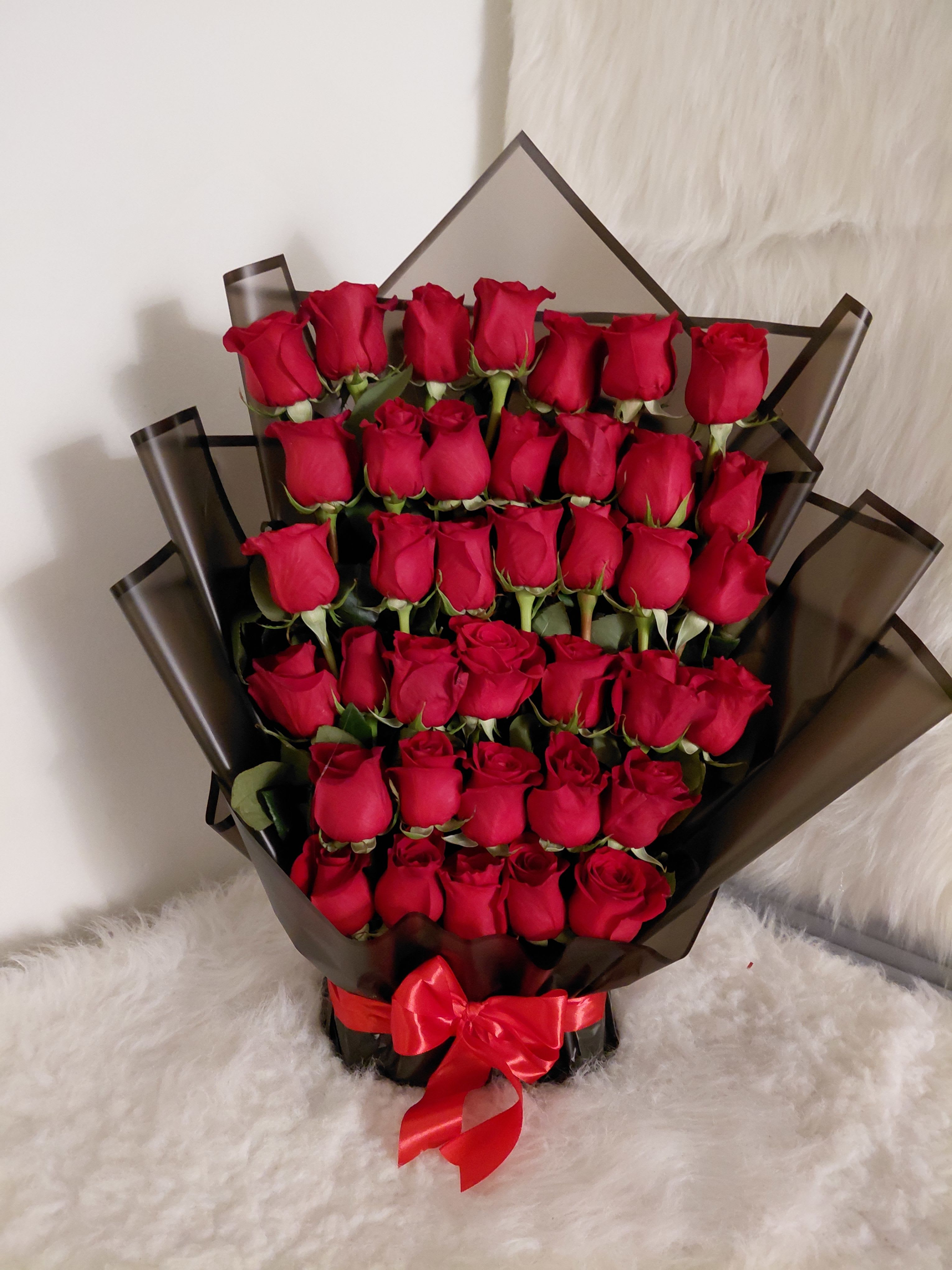 Large bouquet of red roses wrapped in dark paper with a red ribbon