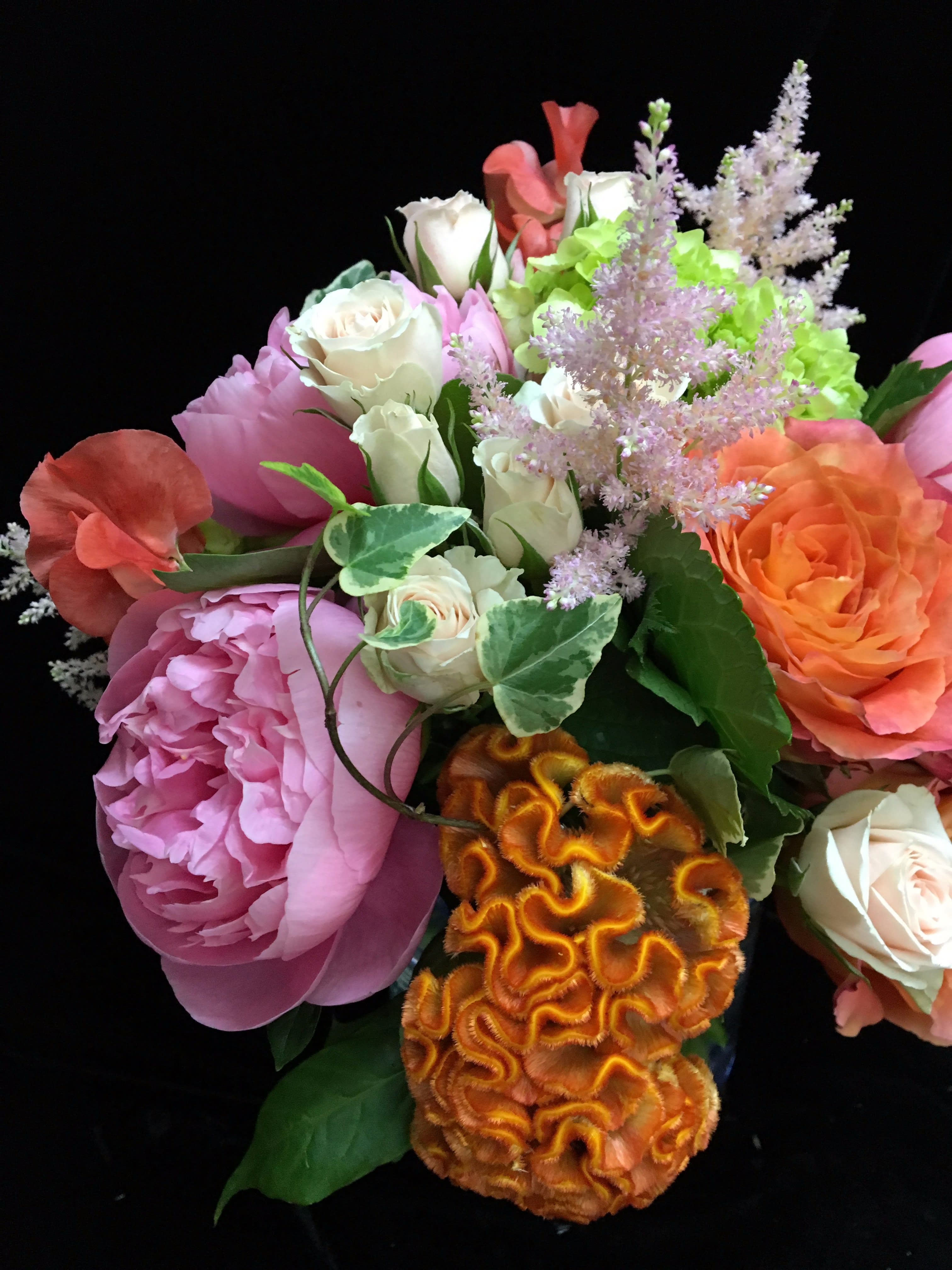 Mixed bouquet with pink peony, cream and orange roses, green hydrangea and orange celosia on black background