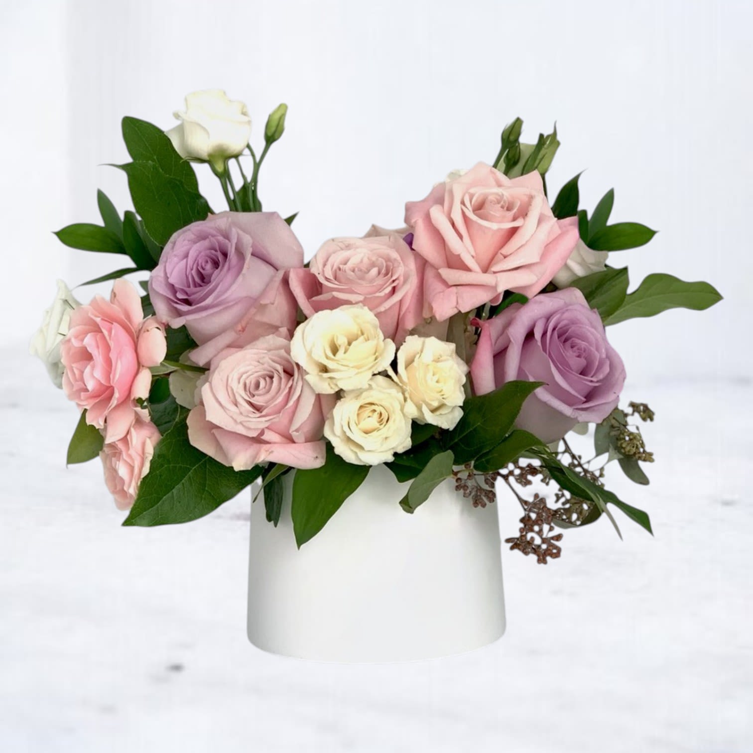 Pink, lavender, and white roses arranged in a white vase