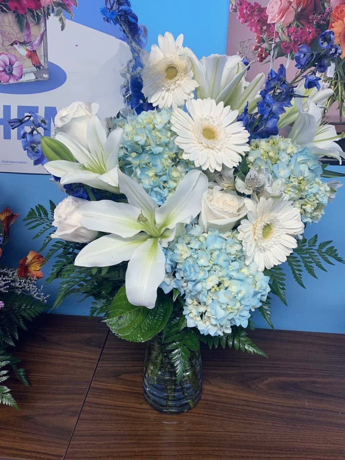 White lilies, gerbera daisies, and blue hydrangeas in a glass vase