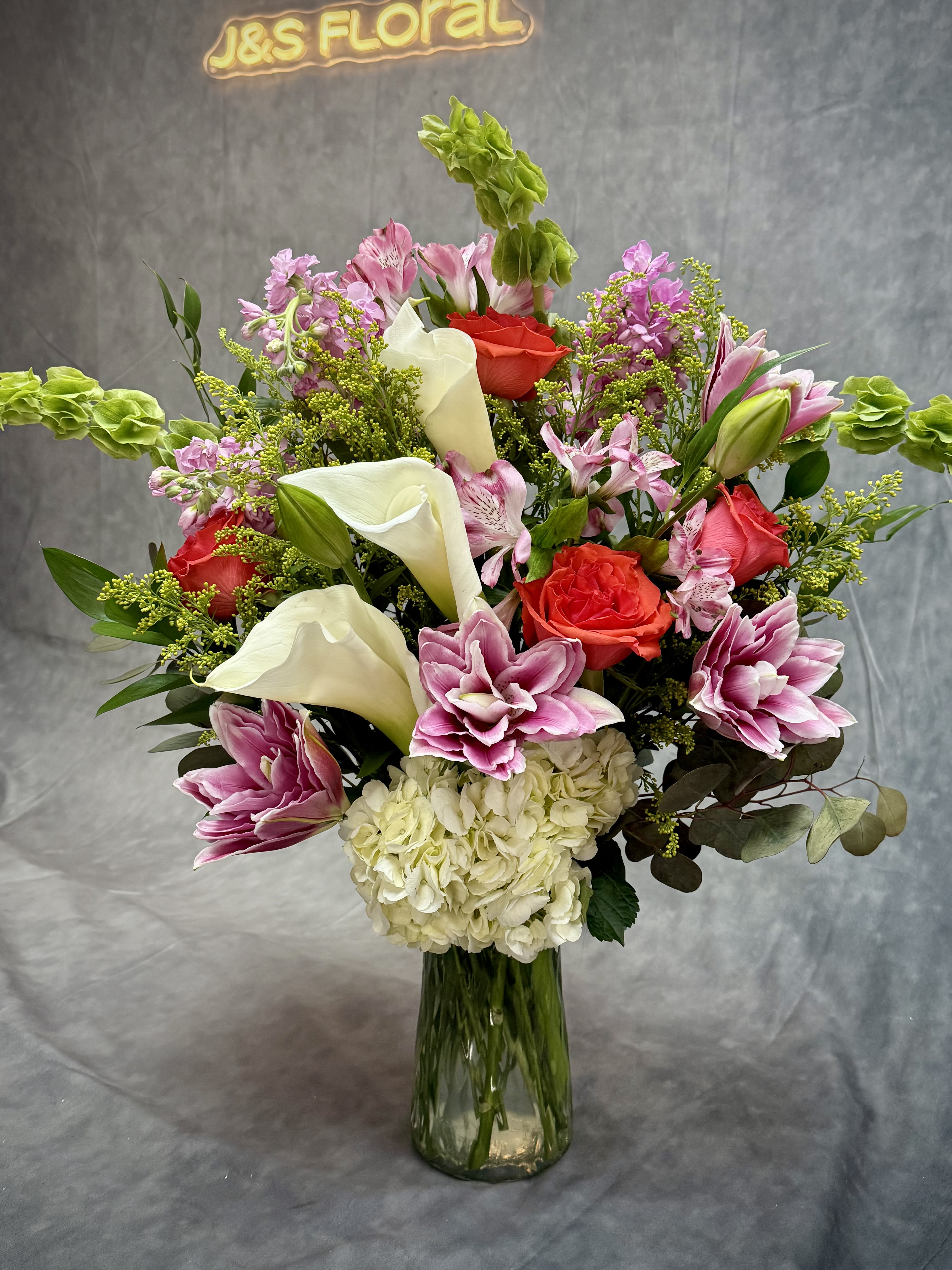 Mixed bouquet with pink lilies, red roses, white calla lilies, and hydrangea in a glass vase