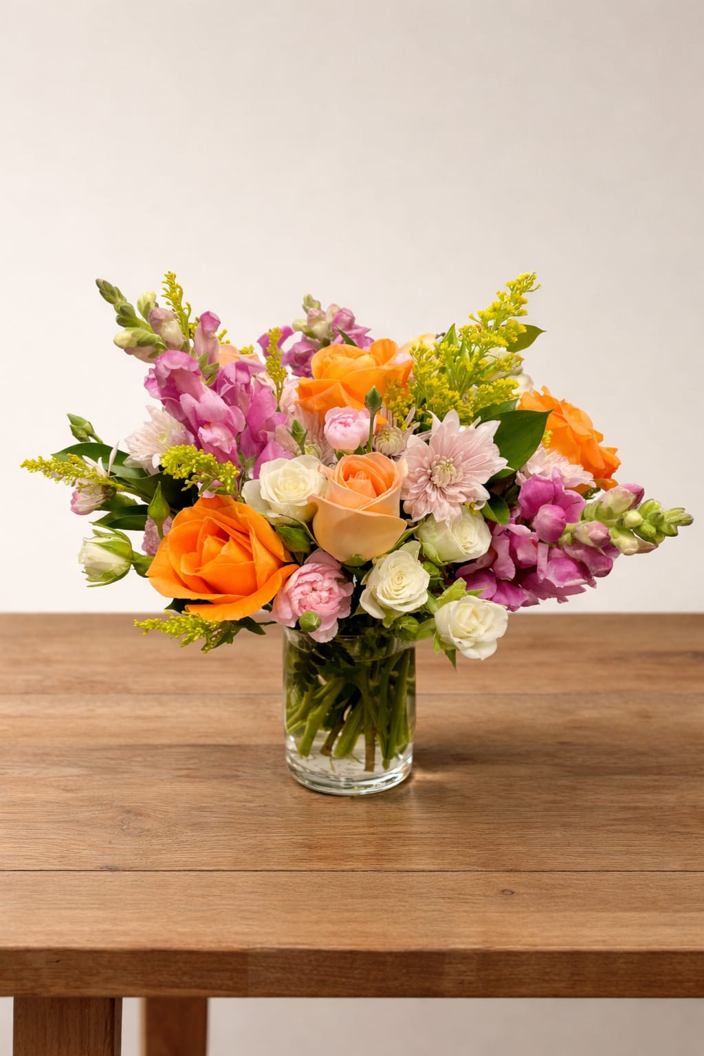 Mixed bouquet of orange, pink, and white flowers in a clear glass vase
