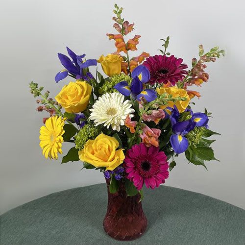 Mixed bouquet of roses, gerbera daisies, irises, and snapdragons in a red vase