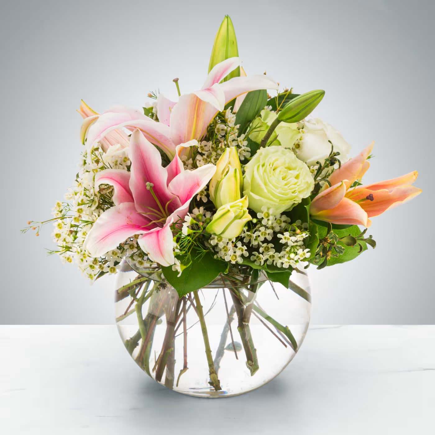 Pink lilies and pale roses in a round glass vase