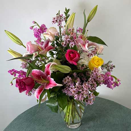 Mixed bouquet of lilies, roses, and small pink flowers in a glass vase