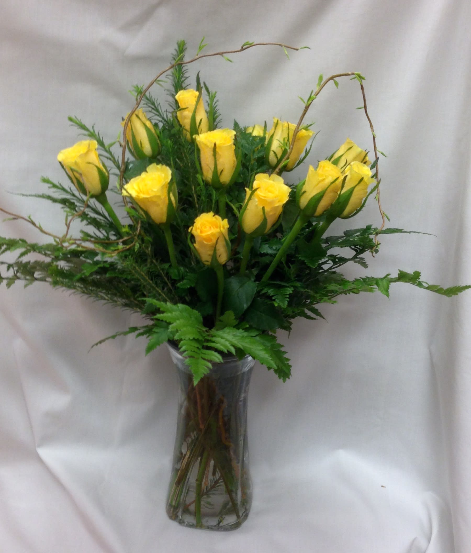 Dozen Yellow Roses with Curly Willow - Premium yellow roses arranged in a clear glass vase with leather leaf greens and curly willow branches. A wondrous display of love, friendship and beauty. Includes 12 roses, and a 8" clear glass vase, all our arrangements are done by hand in the shop before delivery, freshness is guaranteed.  
