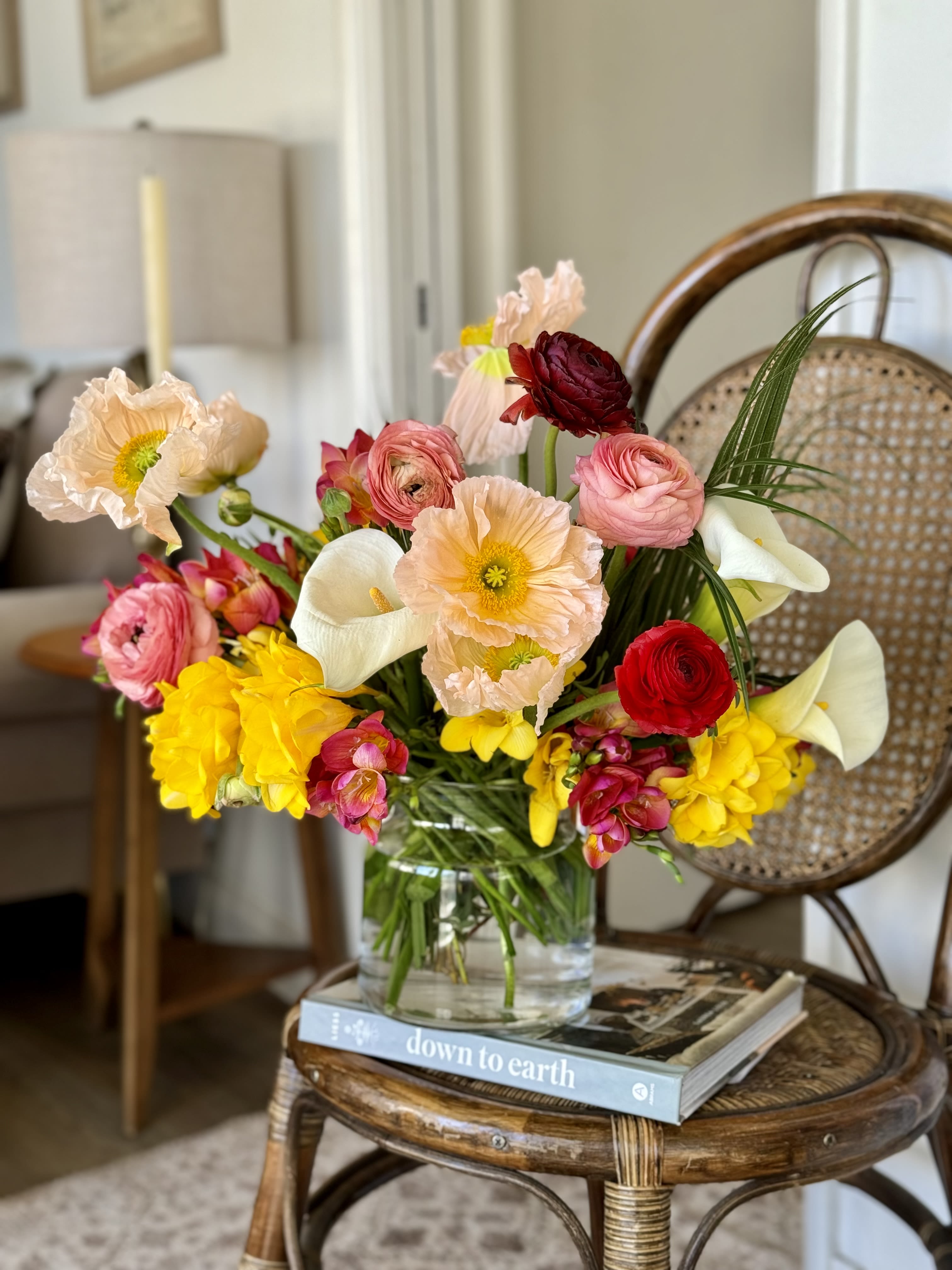 Colorful bouquet in a clear glass vase with poppies, ranunculus, calla lilies, and yellow blooms