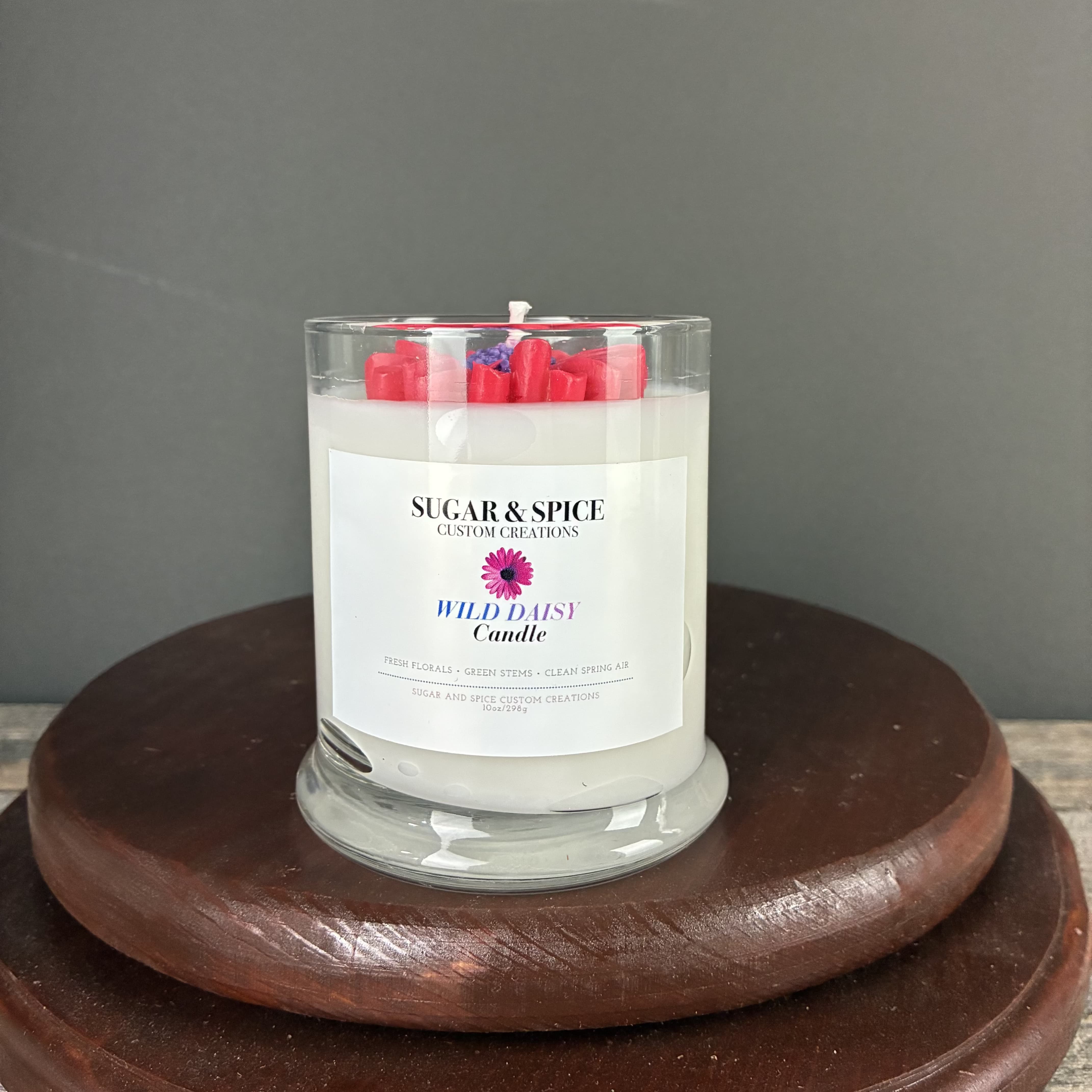 White scented candle in a clear glass jar with red wax accents on a wooden stand