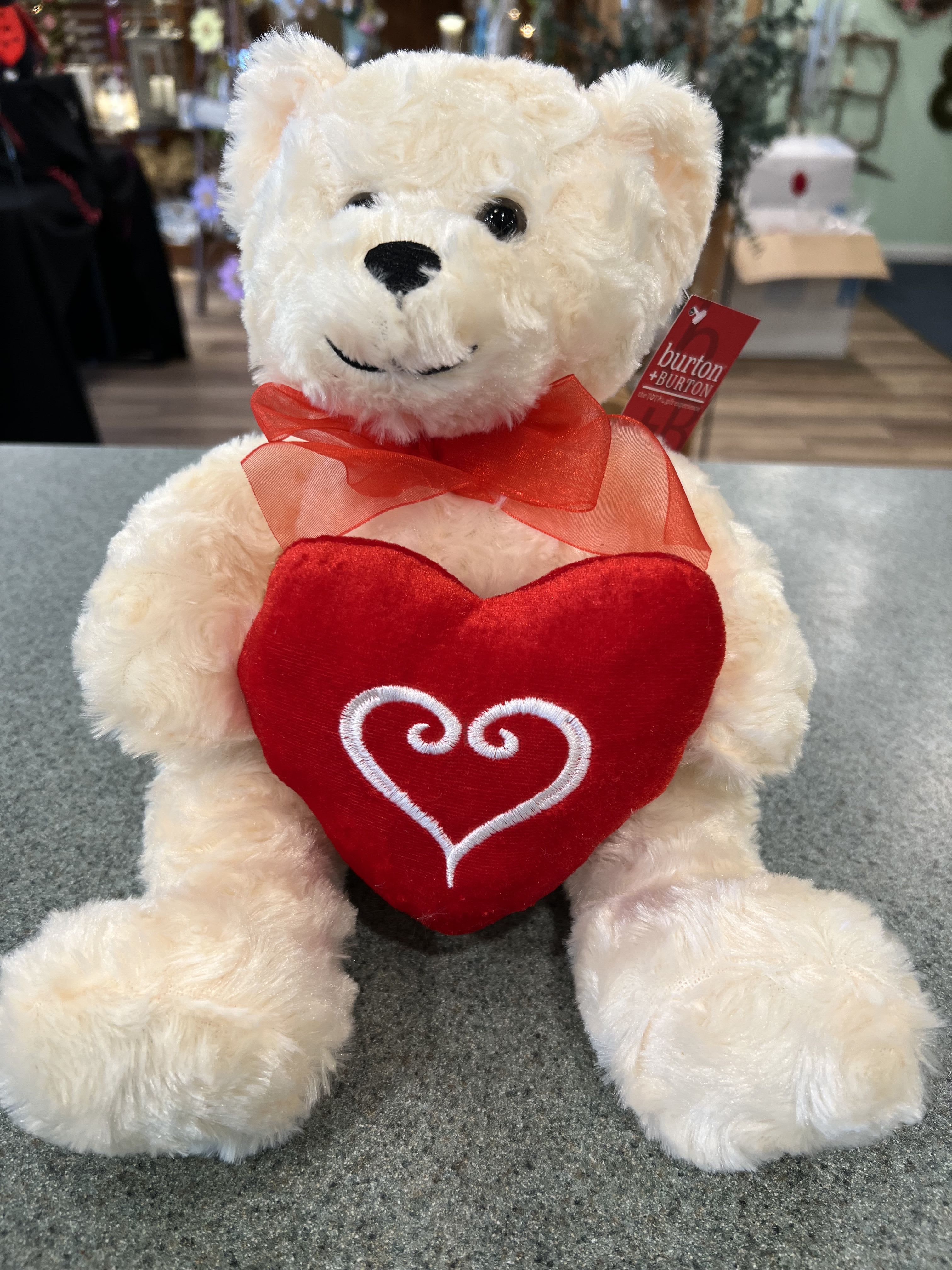 White teddy bear holding a red heart and wearing a red ribbon