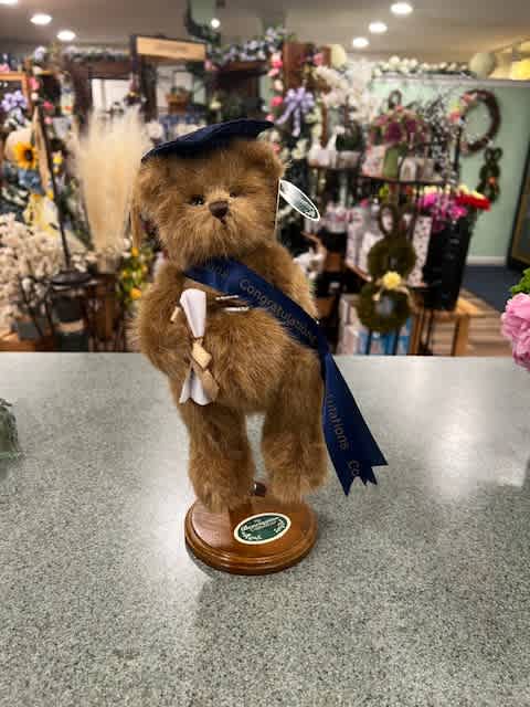 Plush teddy bear figurine on a wooden base with a graduation ribbon