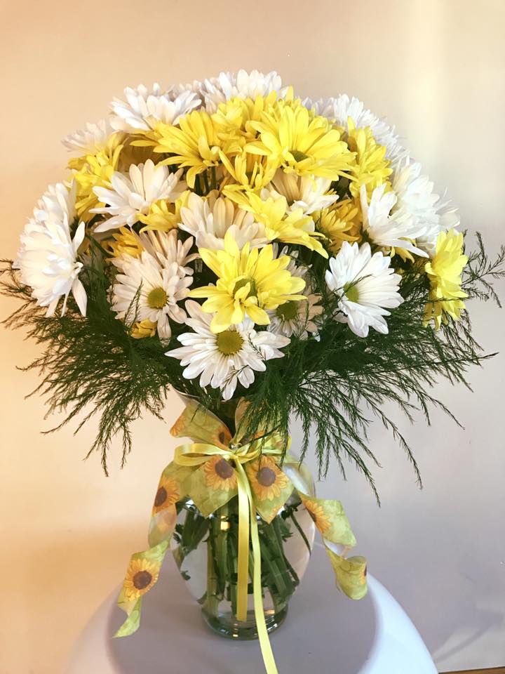 Yellow and white daisy bouquet in a glass vase with a ribbon