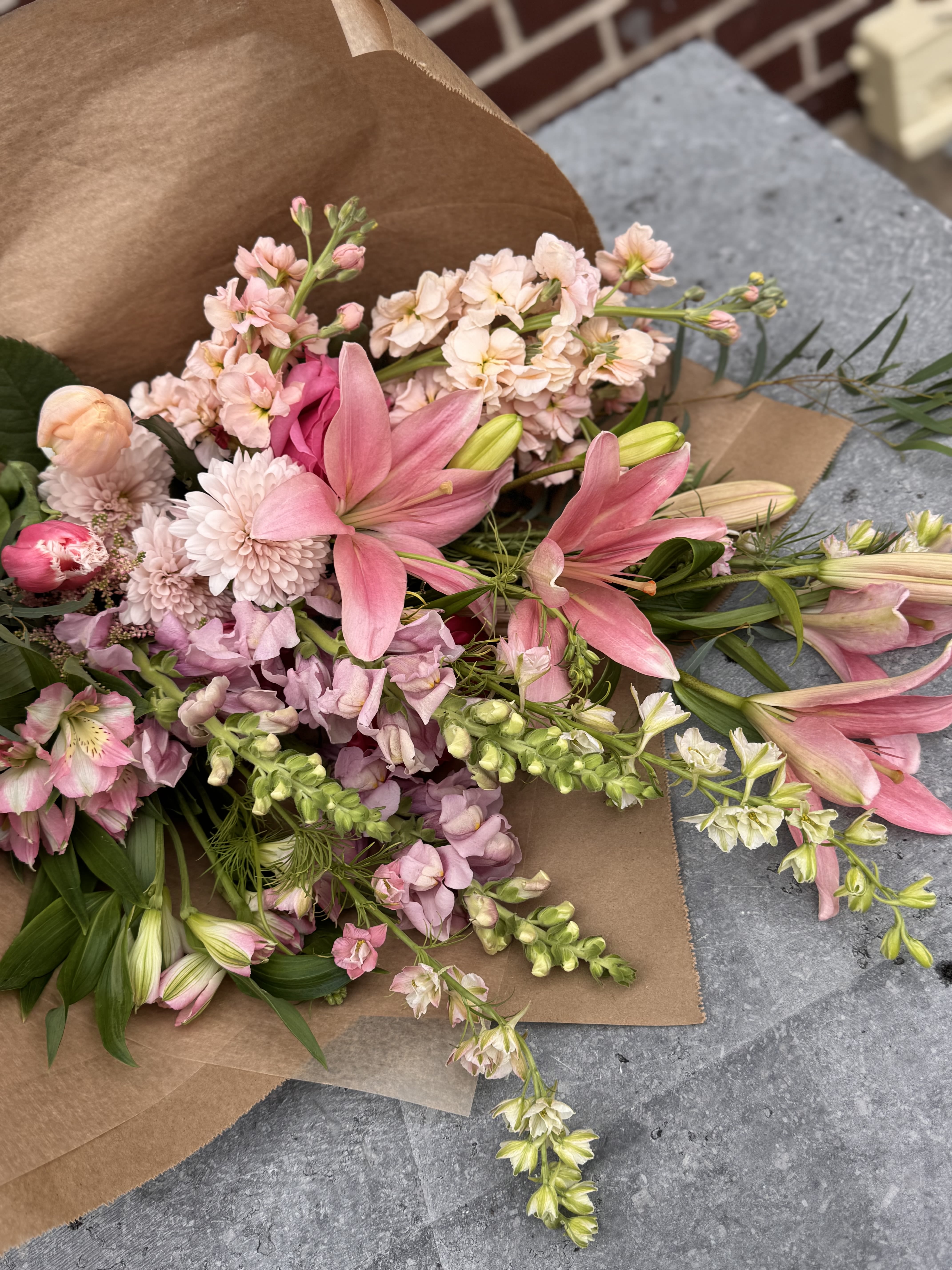 (Mother's Day) Loose Wrap Bouquet - Our Mother’s Day loose wrap bouquets are made to feel effortless and full of life: hand tied with a seasonal mix of fresh blooms in bright, uplifting tones. Each bouquet has a soft, natural movement to it, as if it’s just been gathered from the garden. No two are exactly alike, but all are designed with the same care and intention.  We offer three sizes, each one growing in presence and fullness, layered with more stems, texture, and variety as they scale. Whether you’re drawn to something light and simple or a more generous, abundant bundle, there’s a version that will feel just right in hand.  This offering is meant for more than just one kind of relationship. Whether you’re celebrating a mother, honoring someone who stepped into that role, showing love to a friend, or holding space for something more complicated—estrangement, loss, or distance—these bouquets are created with sensitivity to all of it. You don’t have to explain the gesture for it to matter.  If you have something more specific in mind or are hoping for a larger bouquet, we’re always happy to create a custom wrap. Reach out by phone or email, and we’ll make something tailored just for you.
