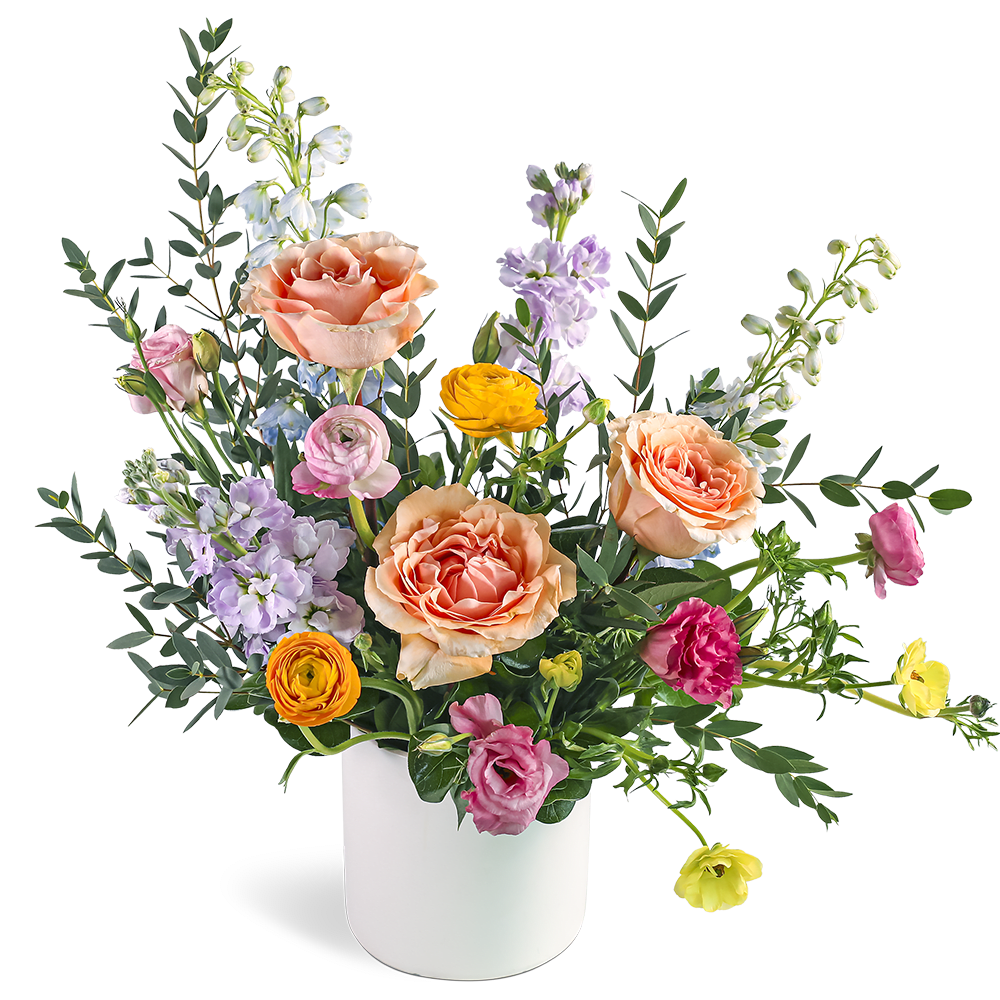 Mixed arrangement of peach roses, ranunculus, and lavender blooms in a white vase