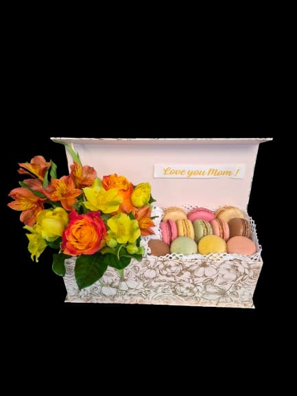 Sweet Mom - Bright clusters of orange roses paired with orange alstroemeria and yellow tulips bring a sunny, affectionate energy to this Mother's Day gift set - a cheerful gift box and macarons combo perfect for a birthday or to say "I'm thinking of you." The compact presentation feels celebratory and personal, with a small printed card that reads "Love you Mom!" to make the recipient feel truly seen and loved.  The arrangement sits on one side of a patterned white decorative gift box, the blooms accented by pink and white highlights against a soft paper liner and finished with a ribbon label. On the other side, a tray of pastel macarons adds a delicate texture and taste contrast to the vivid floral colors; the mixed-color palette of pink, orange, yellow and white makes the set bright and versatile for spring or any joyful occasion.  Designed as a ready-to-gift keepsake, this set is ideal for moms, grandmothers, or anyone who deserves a sunny surprise - it reads as both thoughtful and festive. The compact box is presentation-ready; keep flowers in a cool spot away from direct sunlight and enjoy the macarons fresh from the tray for best flavor.