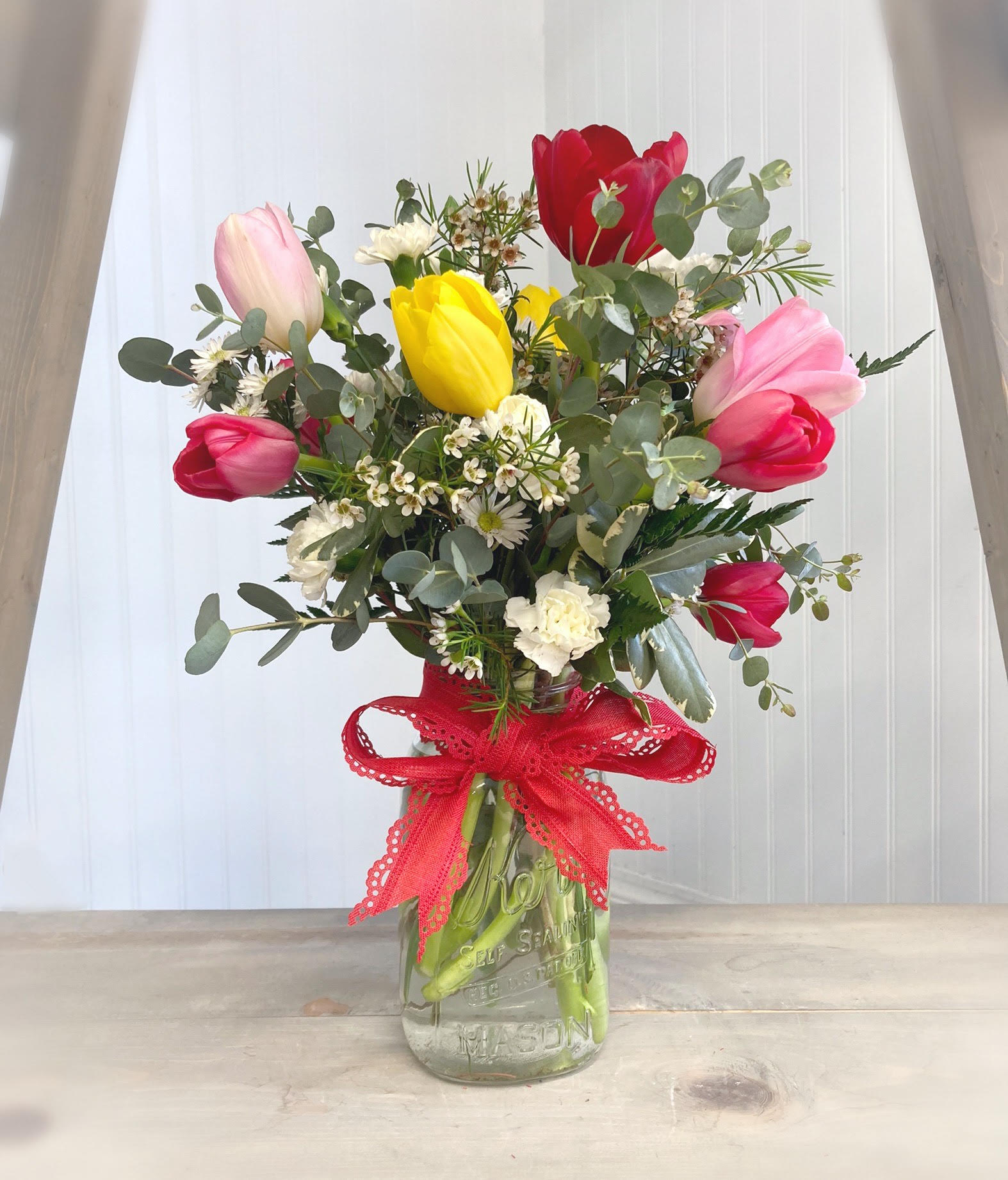 Bouquet of colorful tulips in a glass jar with a red ribbon