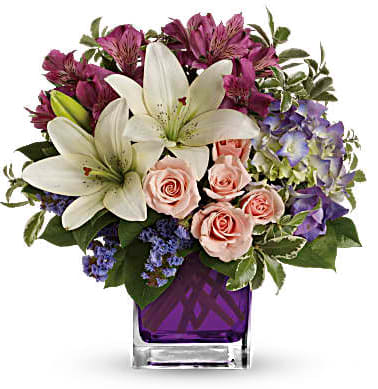 Bouquet of white lilies, pink roses, and purple flowers in a purple vase
