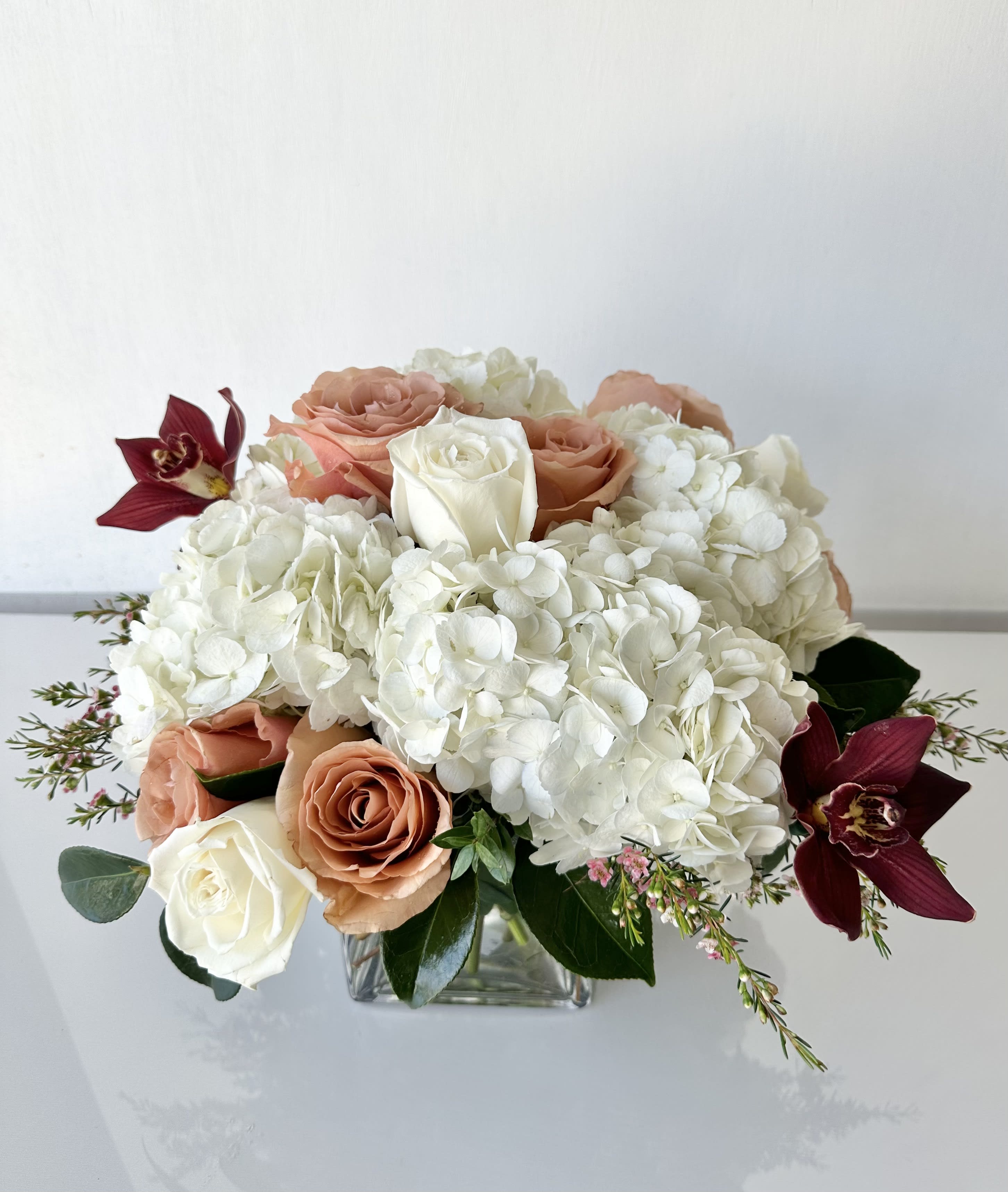 Blooms of Joy - An elegant arrangement of hydrangeas, roses, and cymbidium orchids in a 5" x 5" glass cube vase. Dimensions: 12" H x 15" W