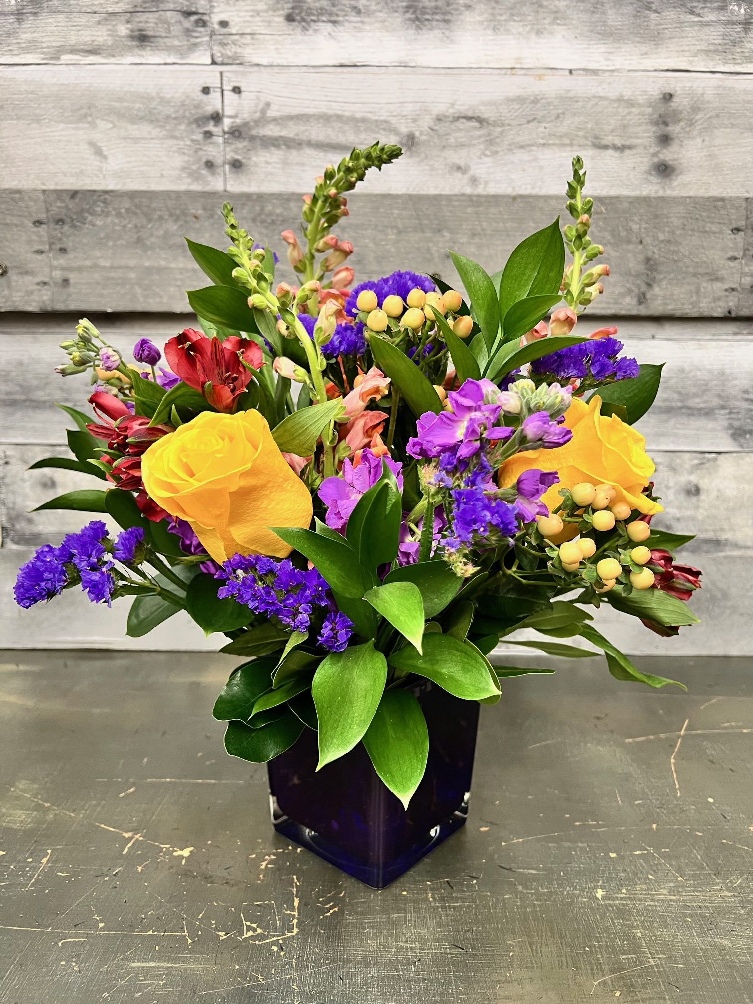 Mixed bouquet with yellow roses and purple flowers in a dark vase