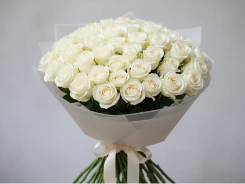 Bouquet of white roses wrapped in pale paper with a ribbon