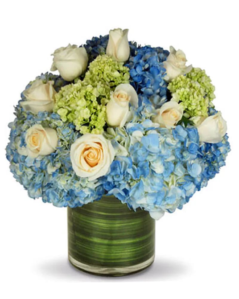 Blue hydrangeas and white roses arranged in a green glass vase