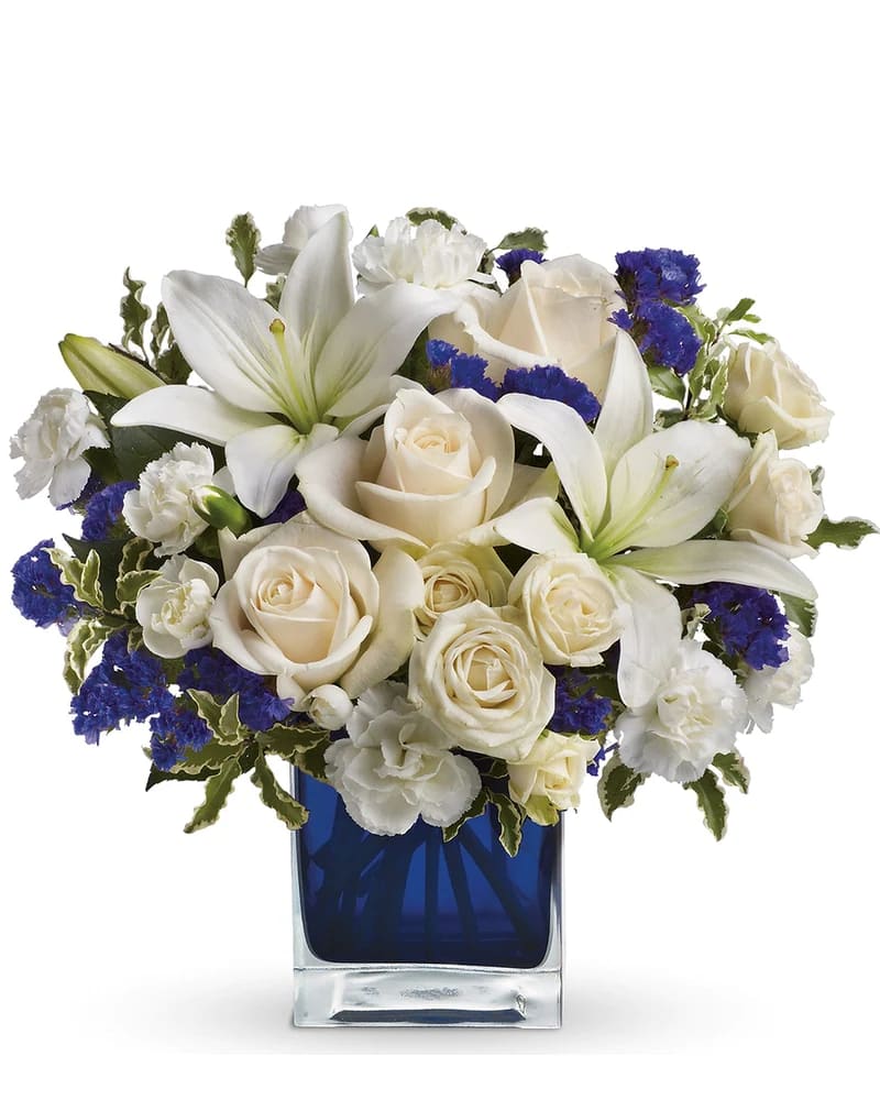White roses and lilies arranged in a blue glass vase