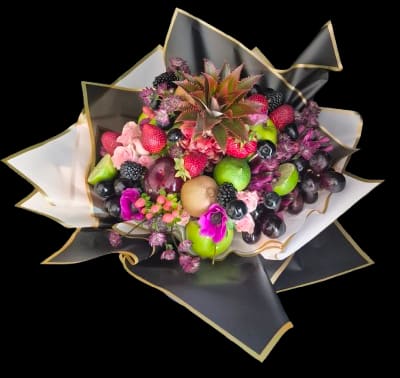 Kiss of Abundance - A playful, gift-like flower arrangement that reads as an abundant edible surprise-perfect as a birthday bouquet, thank-you gift, or special-occasion surprise. Kiss of Abundance pairs a dense, rounded fruit display with floral accents so the recipient feels delight and wonder the moment they unwrap it; pink roses and small purple blossoms peek through clusters of strawberries, grapes, blackberries, apples and a halved lime, while a pineapple crown rises in the center for a spirited focal point.  The color story mixes pink, purple and green fruit tones against dramatic black wrapping paper trimmed in gold, creating an upscale, celebratory contrast. Decorative wrapping paper and additional decorative wrapping finish the presentation, making this arrangement look ready for gifting straight from the shop. The compact, tightly clustered composition emphasizes texture-the smoothness of berries, the spiky pineapple crown and the soft rose petals-so it reads as both visually rich and deliciously playful.  Designed for gifting, Kiss of Abundance makes the person you're thinking of feel genuinely celebrated-ideal for birthdays, thank-yous, congratulations or any moment that calls for a festive, edible surprise. Order ready-wrapped for immediate presentation; because this is a fresh fruit-forward arrangement, enjoy it soon after delivery for best appearance and freshness.