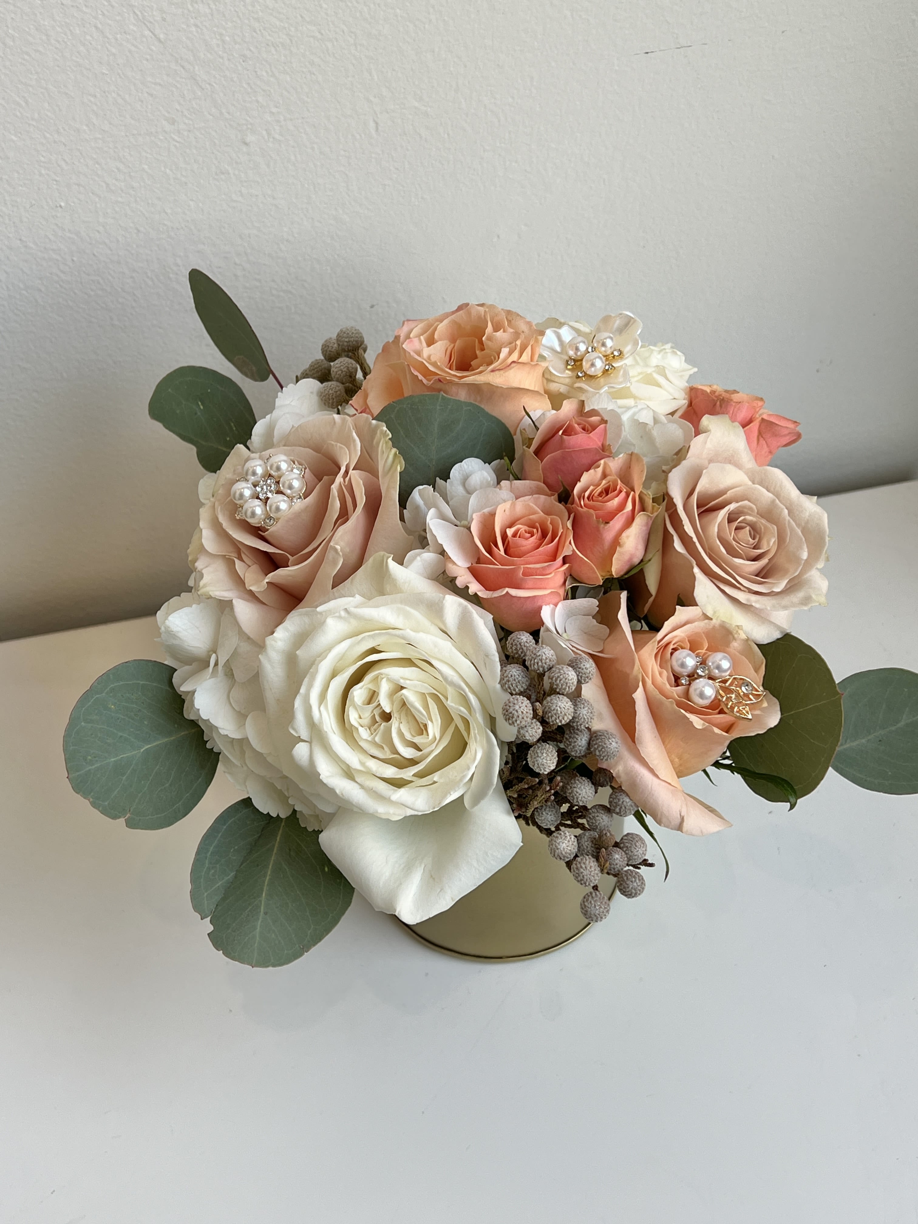 MD26-02 - A Bouquet of Soft Hues of Roses Accented With Pearls, Spray Roses, Hydrangea, Silver Brunia Berries and Silver Dollar Eucalyptus Designed in a Gold Metal Container.