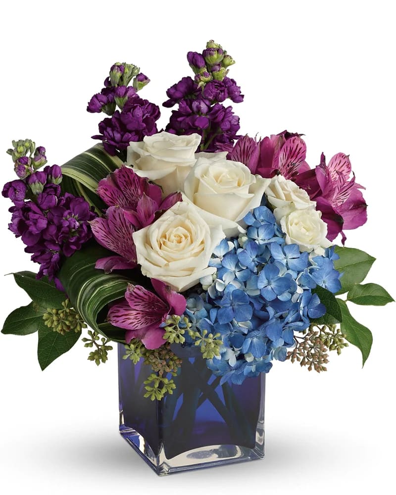 Bouquet of white roses, purple flowers, and blue hydrangea in a square vase