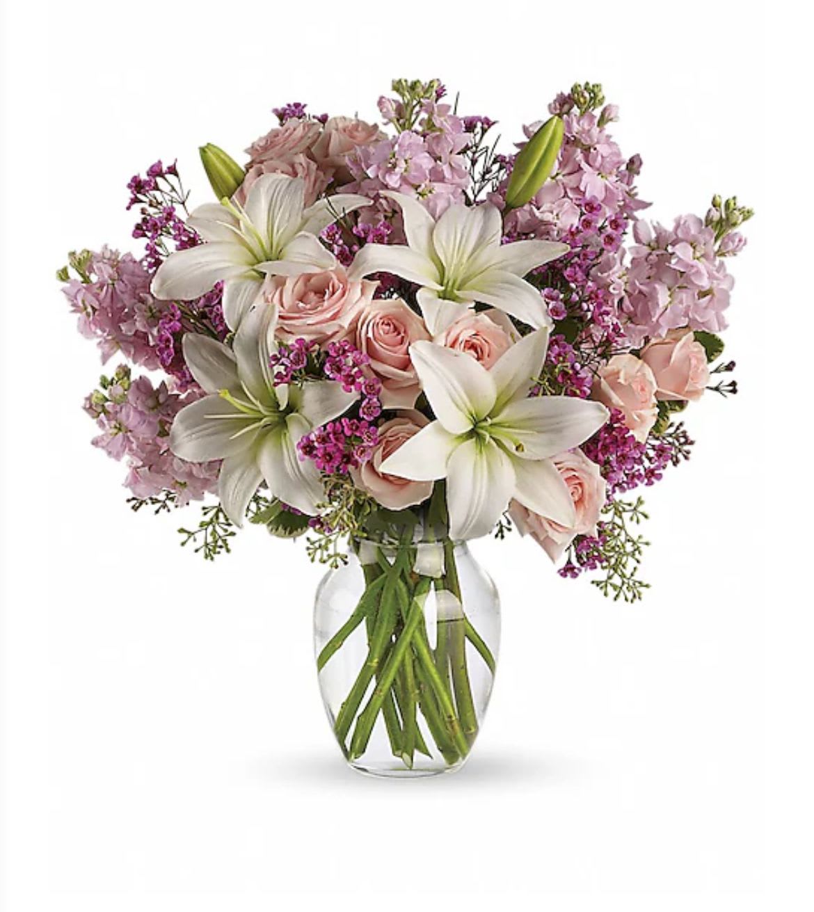 Bouquet of white lilies and light pink roses with purple accents in a clear glass vase
