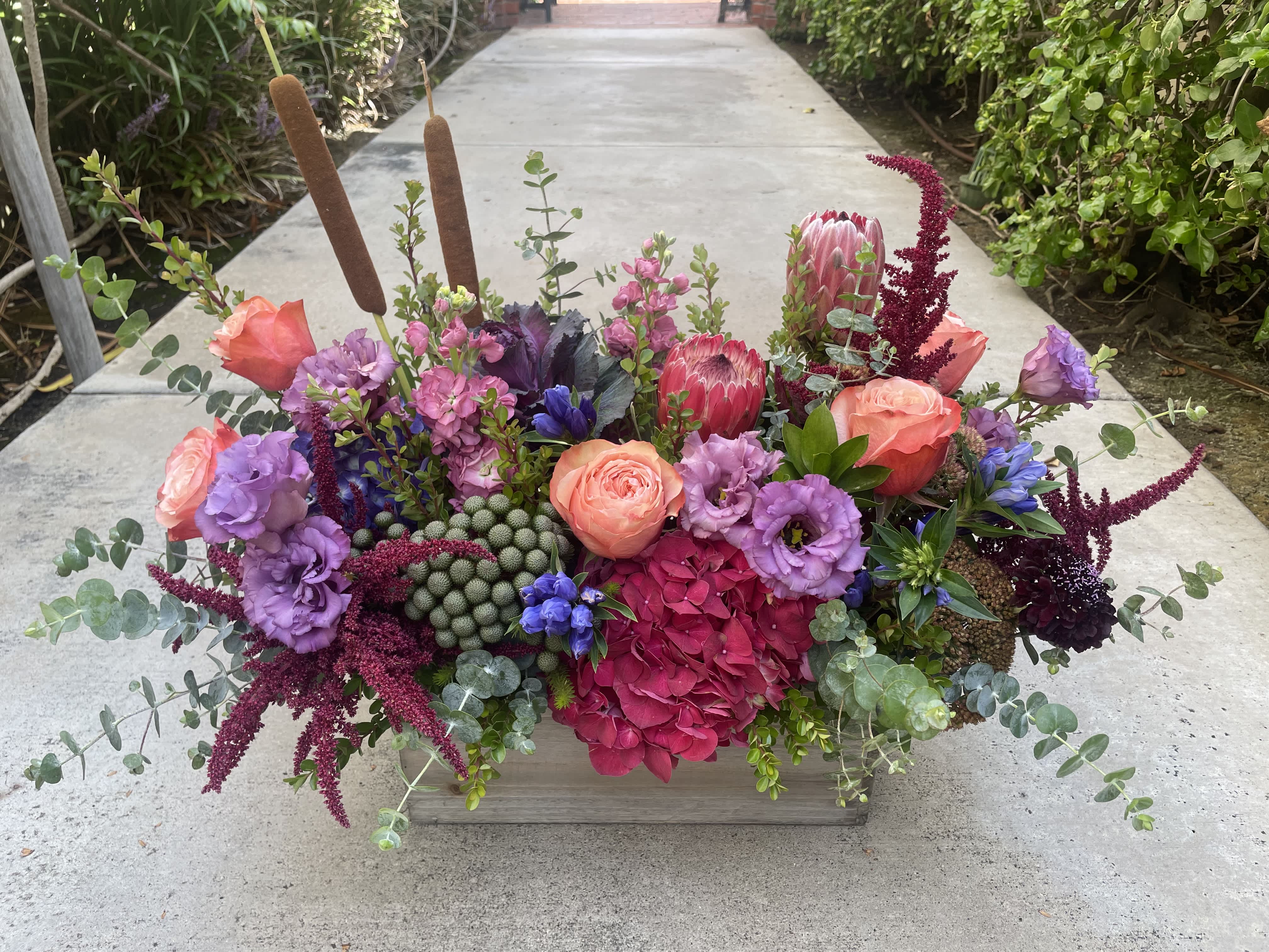 Colorful floral arrangement in a wooden box with pink, purple, and burgundy blooms