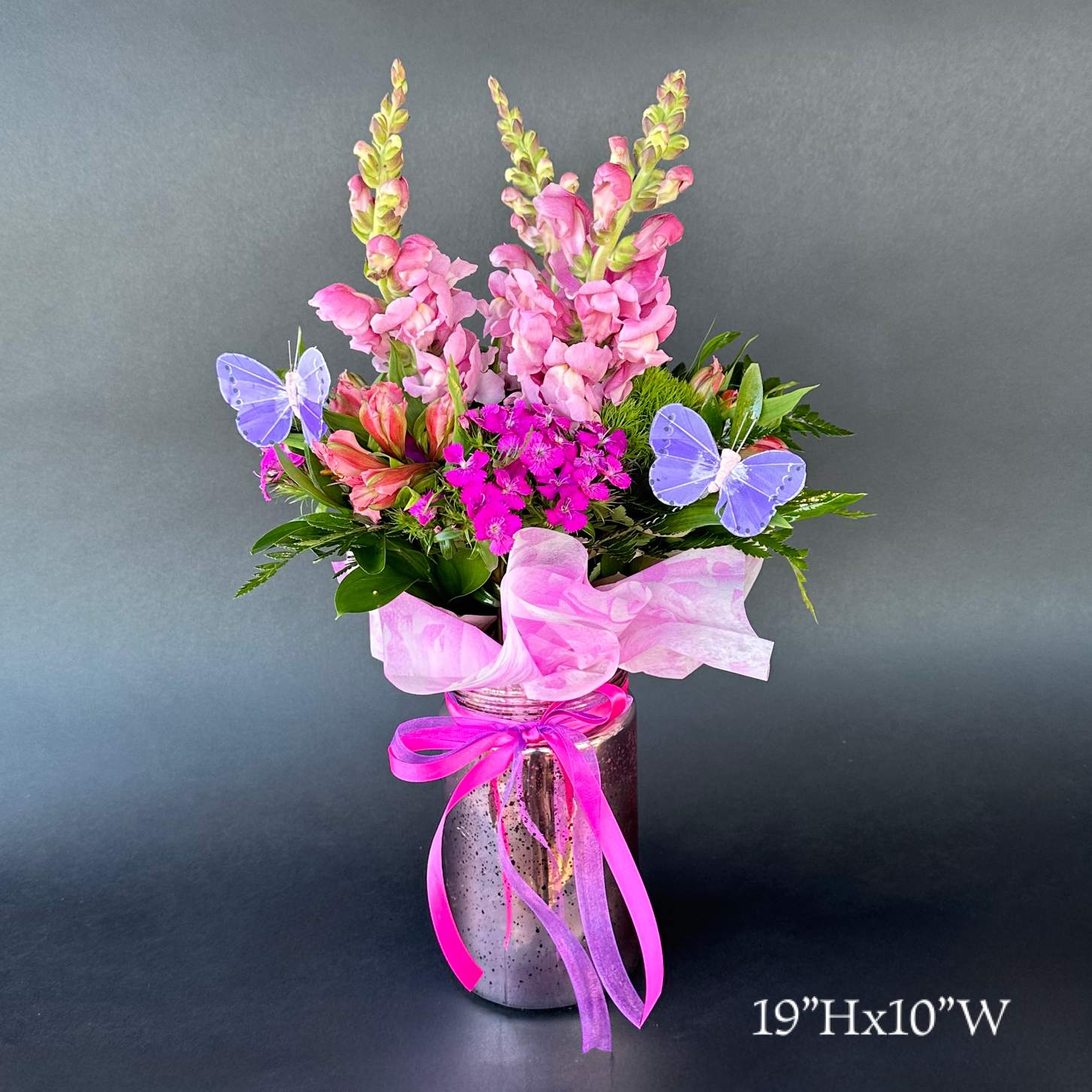 Pink snapdragons and mixed blooms in a glass jar with ribbon and butterfly picks.