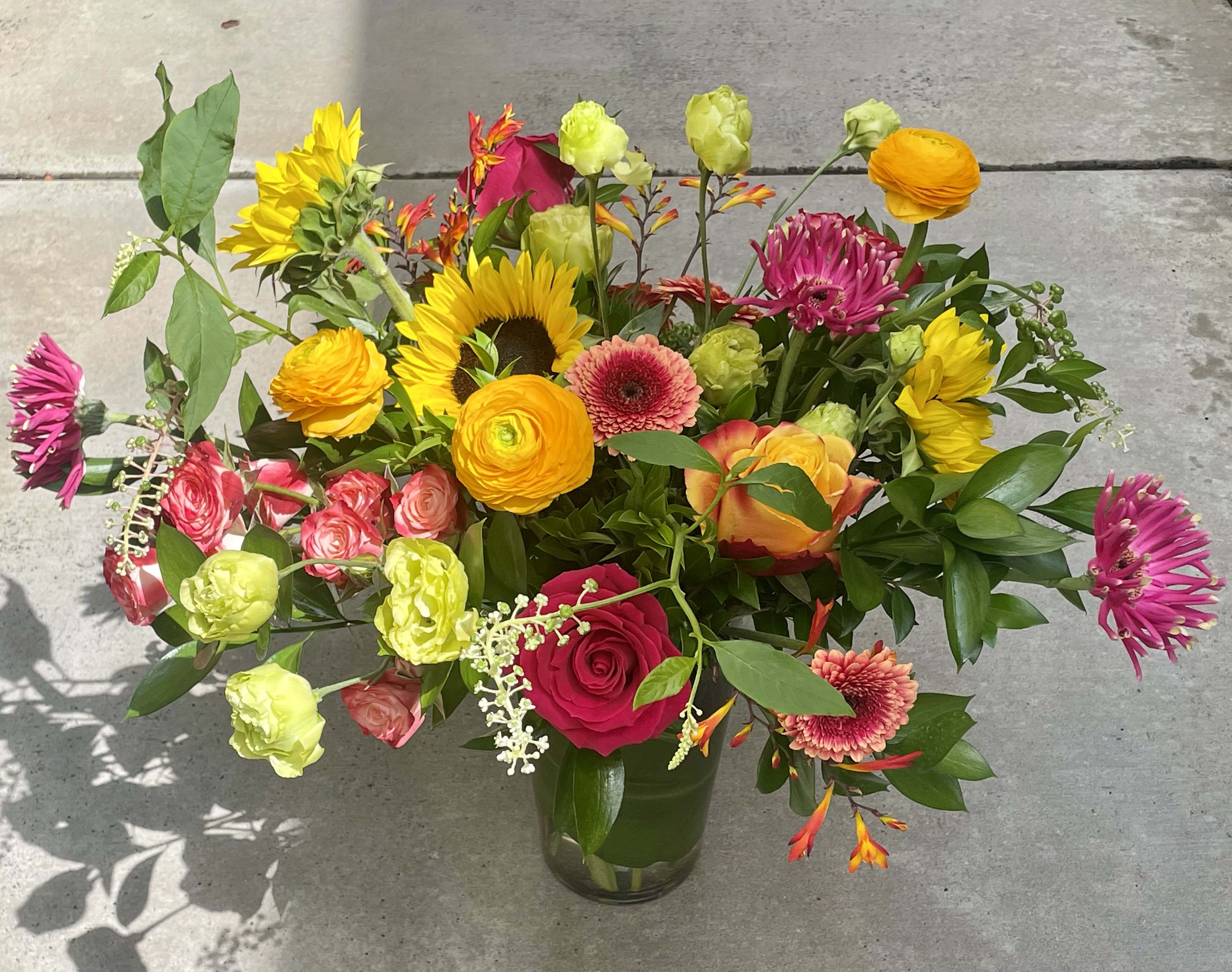 Mixed bouquet in a glass vase with sunflowers, roses, and bright pink blooms