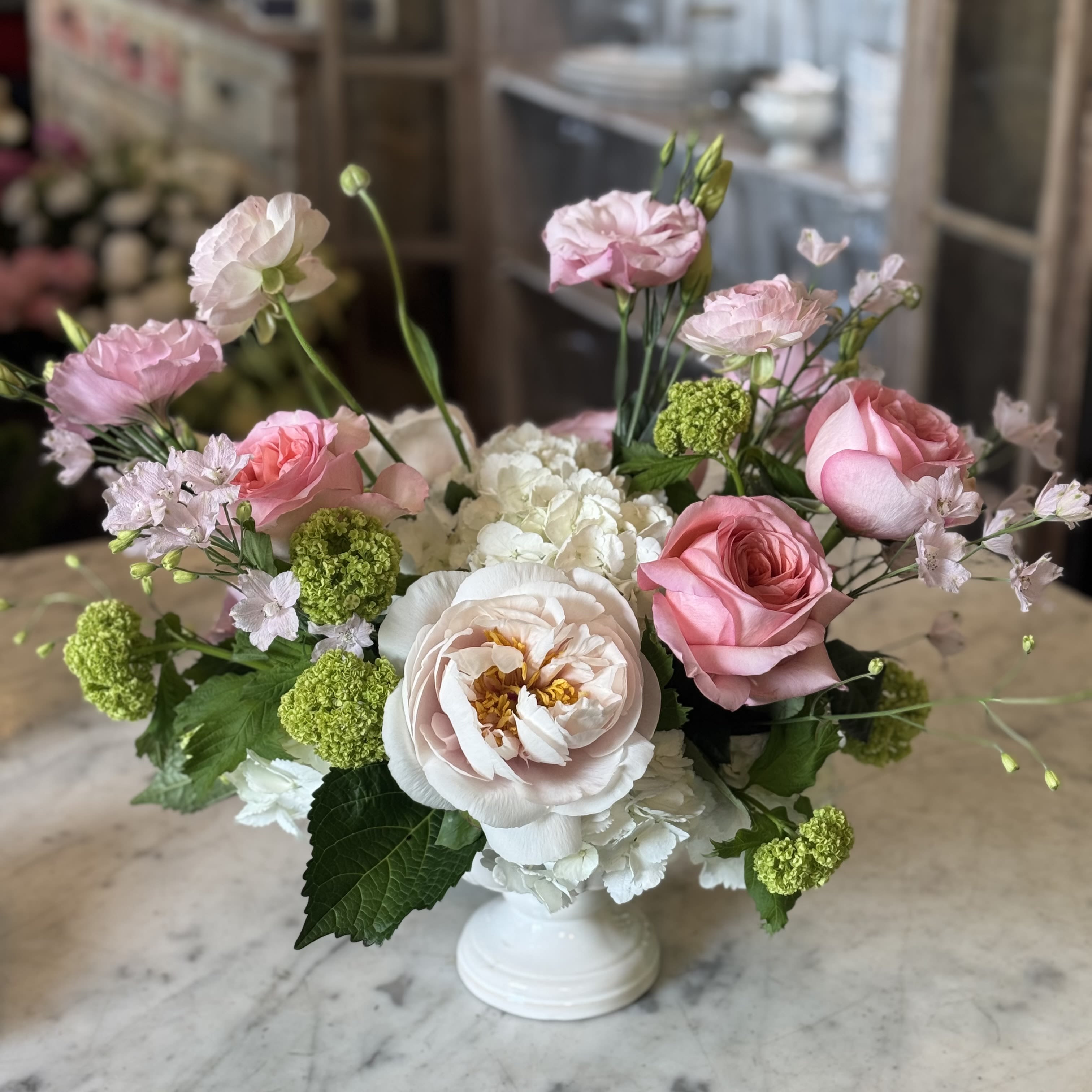 Urban Gardener Mother's Day  - A ceramic footed white pedestal dish filled with white hydrangeas, peony, garden roses, ranunculus, lisianthus and viburnum. Perfect for Mother's Day or any day.