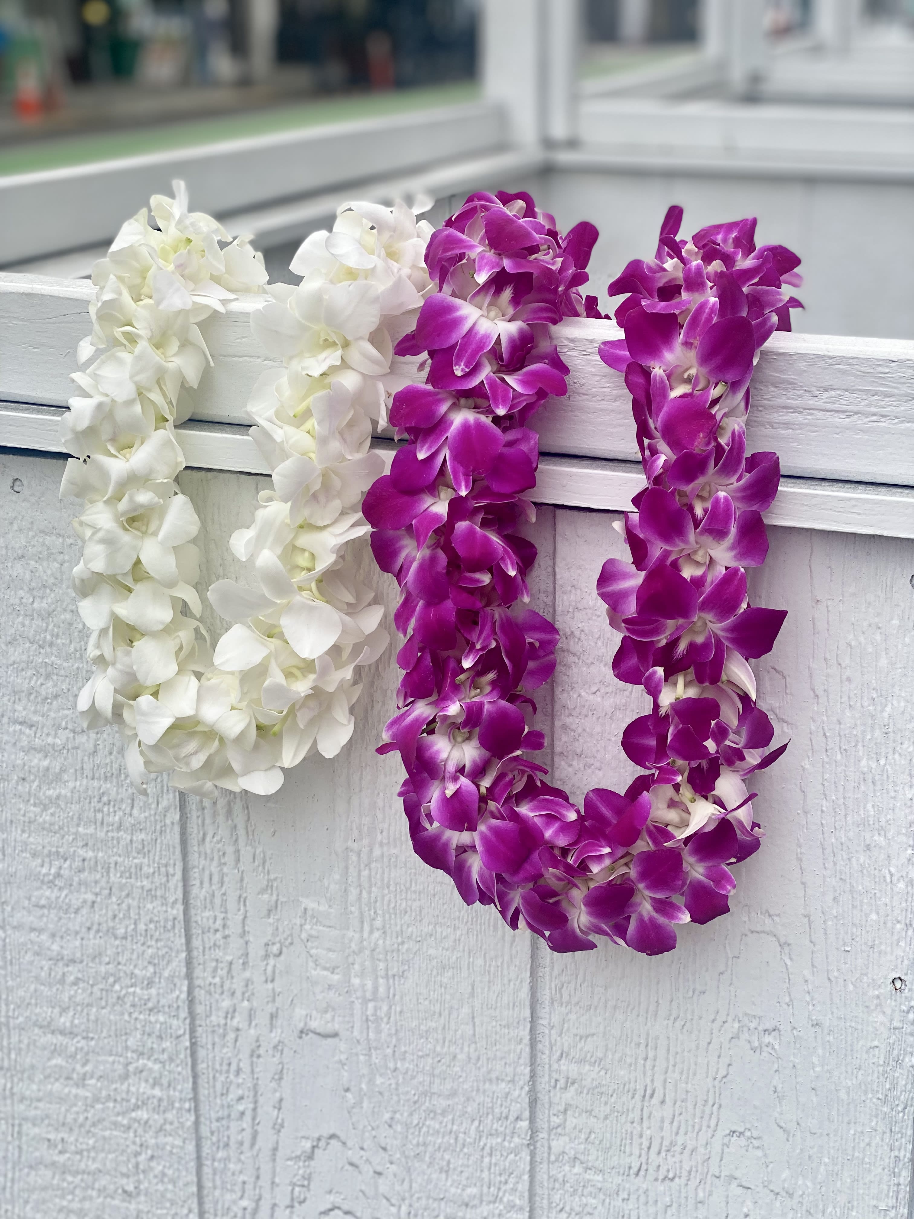 Two orchid leis draped over a white railing, one white and one purple.