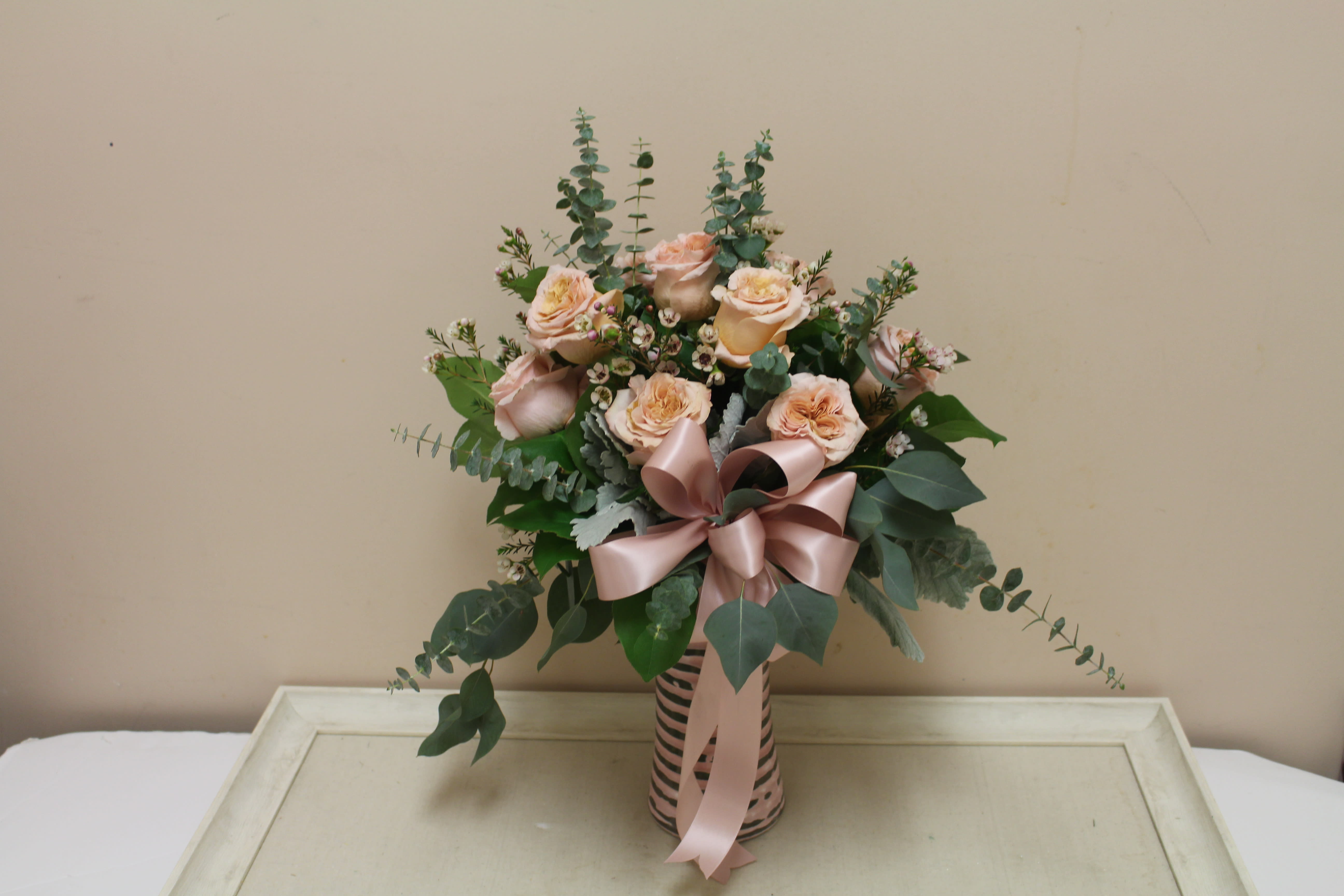 Peach roses in a striped vase with a pink ribbon bow