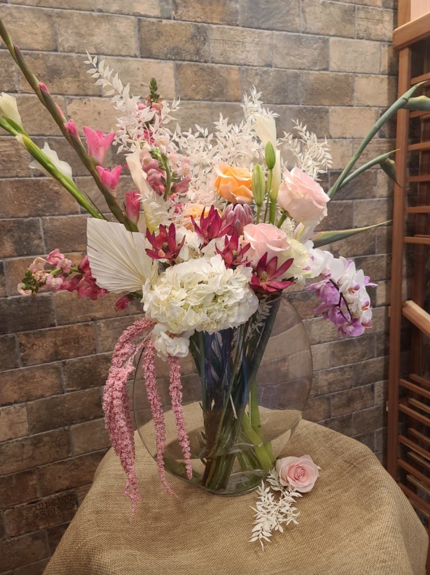Tall mixed bouquet with pink, white, and orange flowers in a clear vase