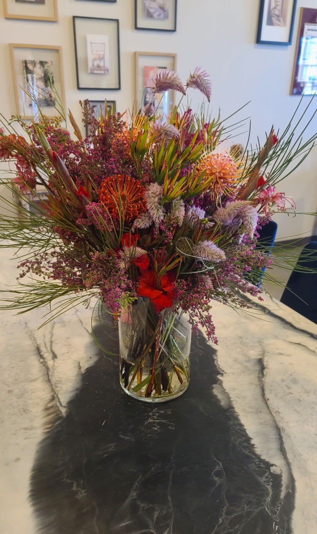 Large mixed bouquet in a clear glass vase with spiky blooms and red accents