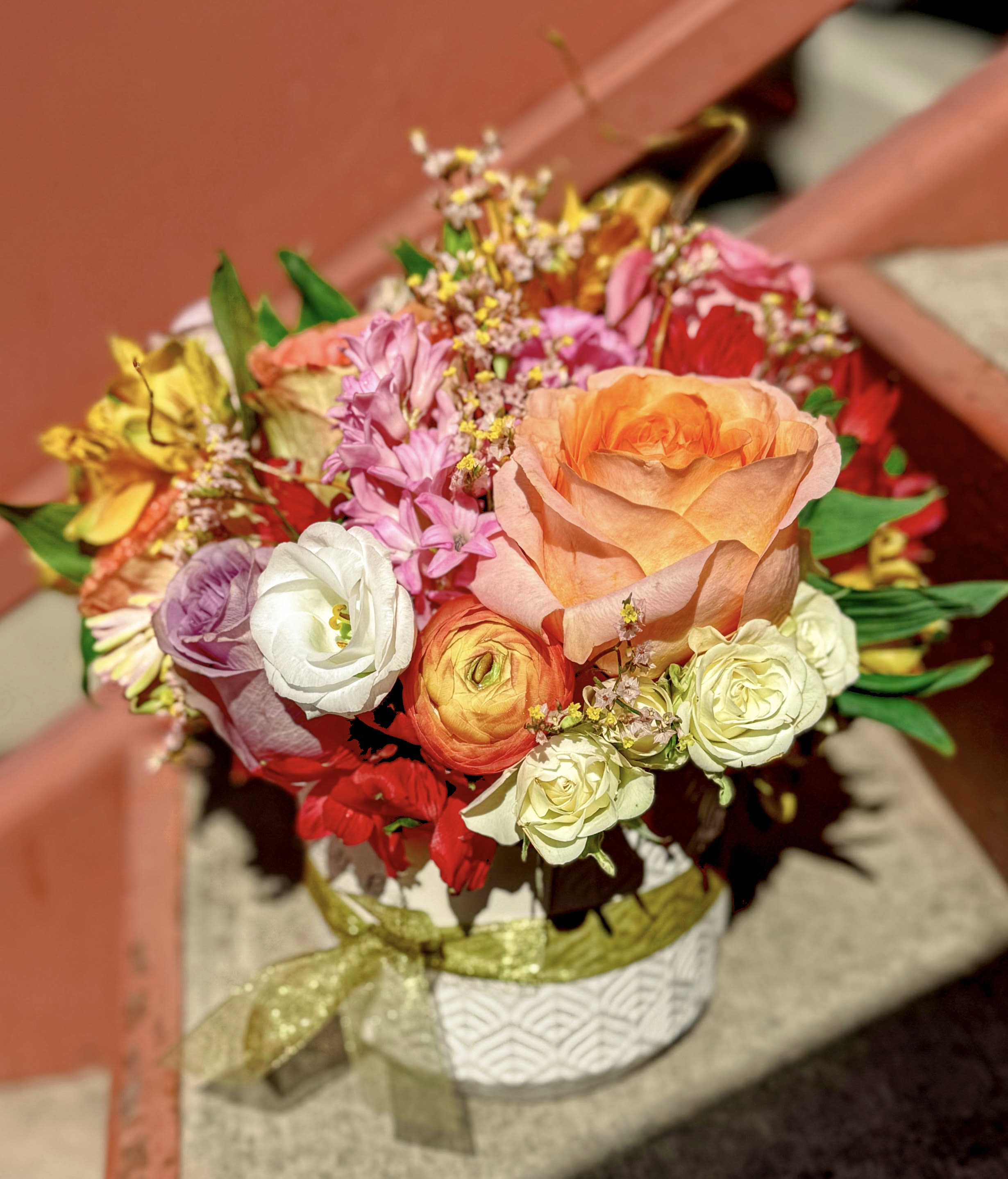 Colorful mixed bouquet with an orange rose and assorted blooms in a white pot with a ribbon bow