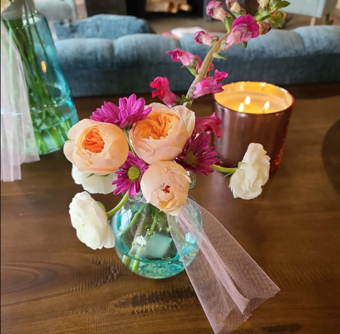 Small bouquet of peach and purple flowers in a blue glass vase with pink tulle